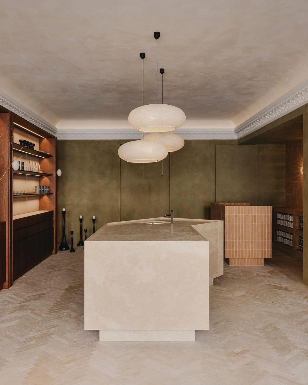 Modern kitchen with beige island, green textured walls, and hanging white paper lantern pendant lights.