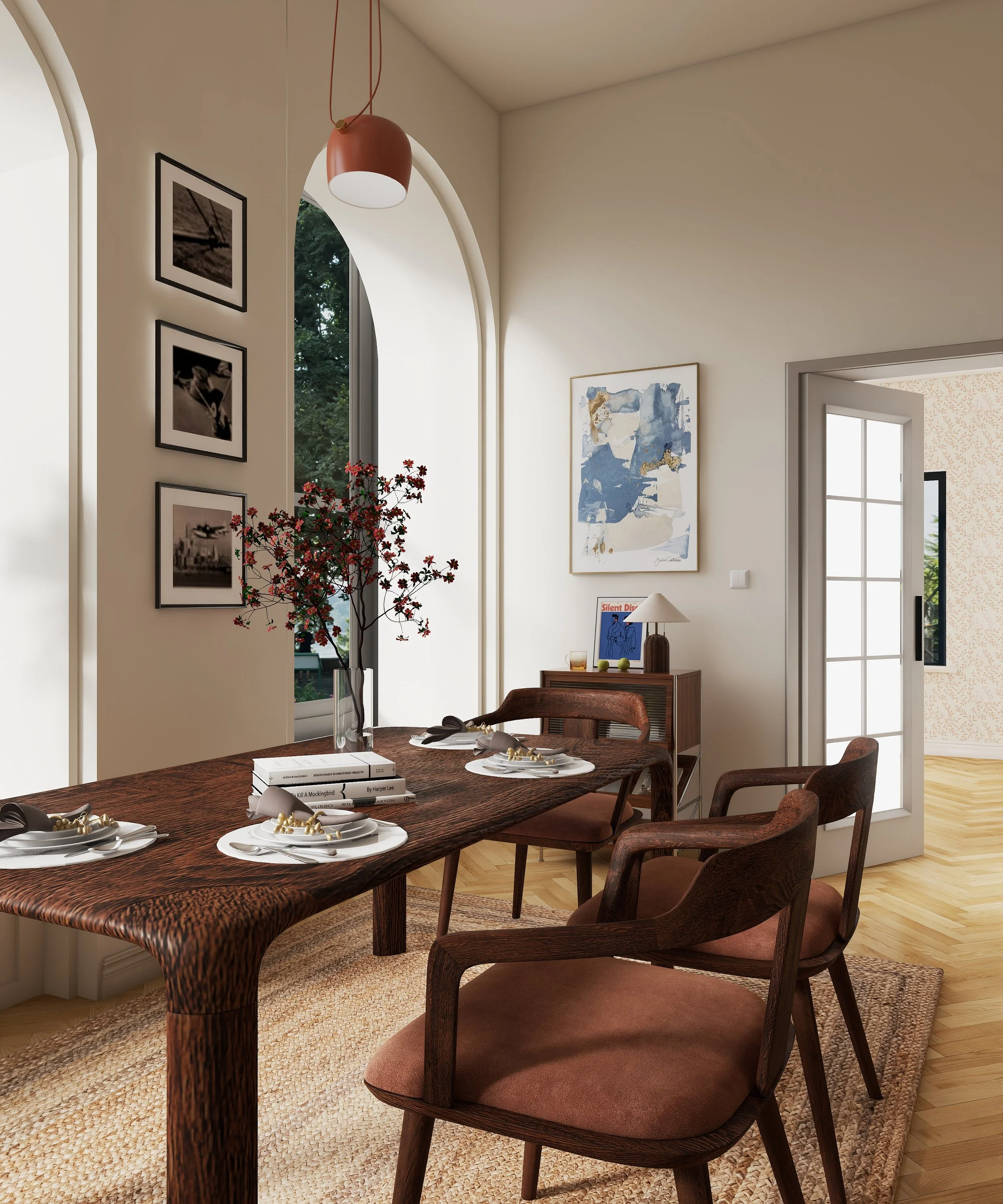 A dining room with a wooden table set with plates, napkins, and decorative items, surrounded by wooden chairs with brown cushions, a window with arched top, wall art, and a sideboard with a table lamp and books.