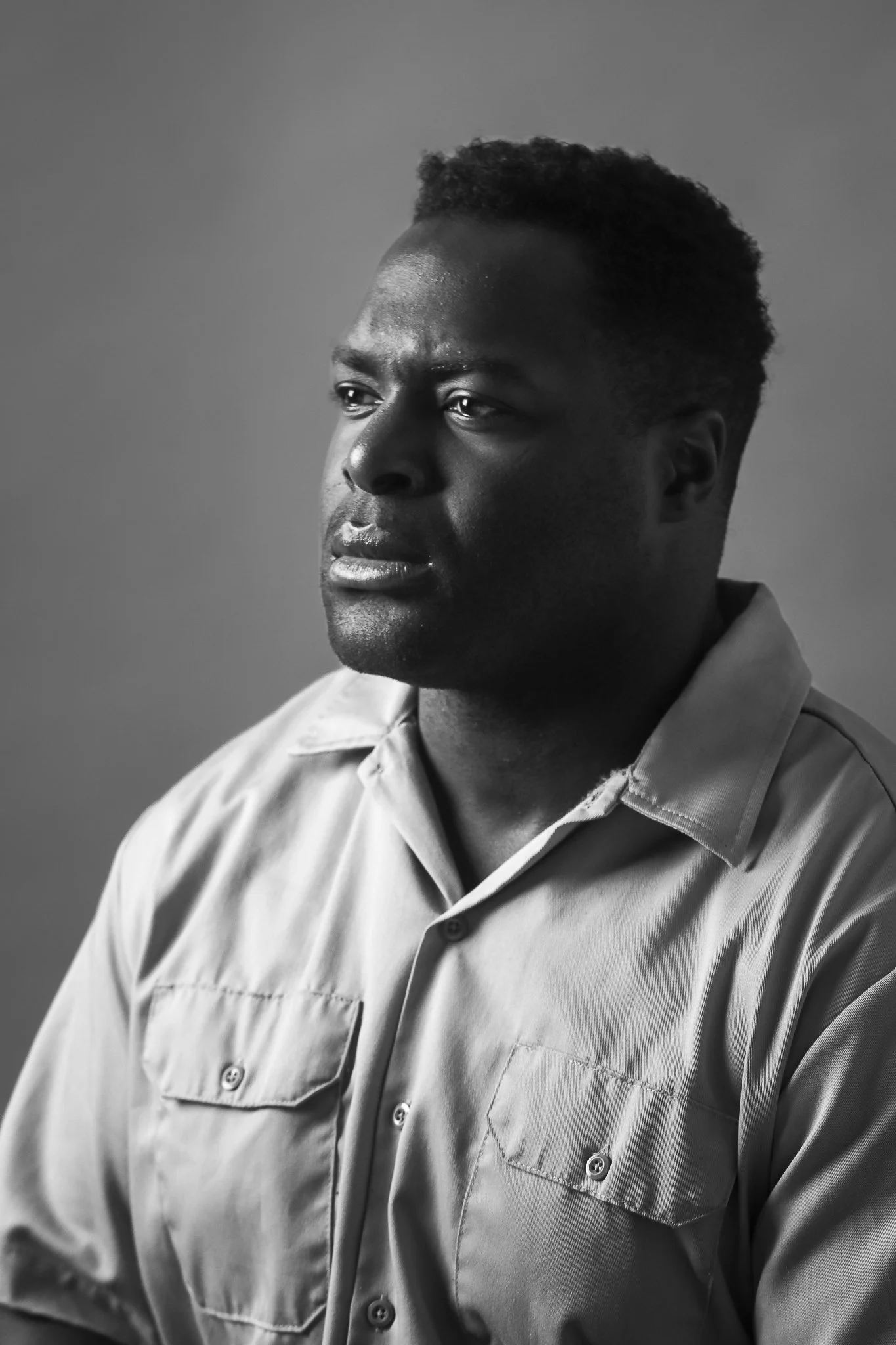 A black and white portrait of an African American man with short, curly hair, wearing a button-down shirt, looking off to the side with a serious expression.