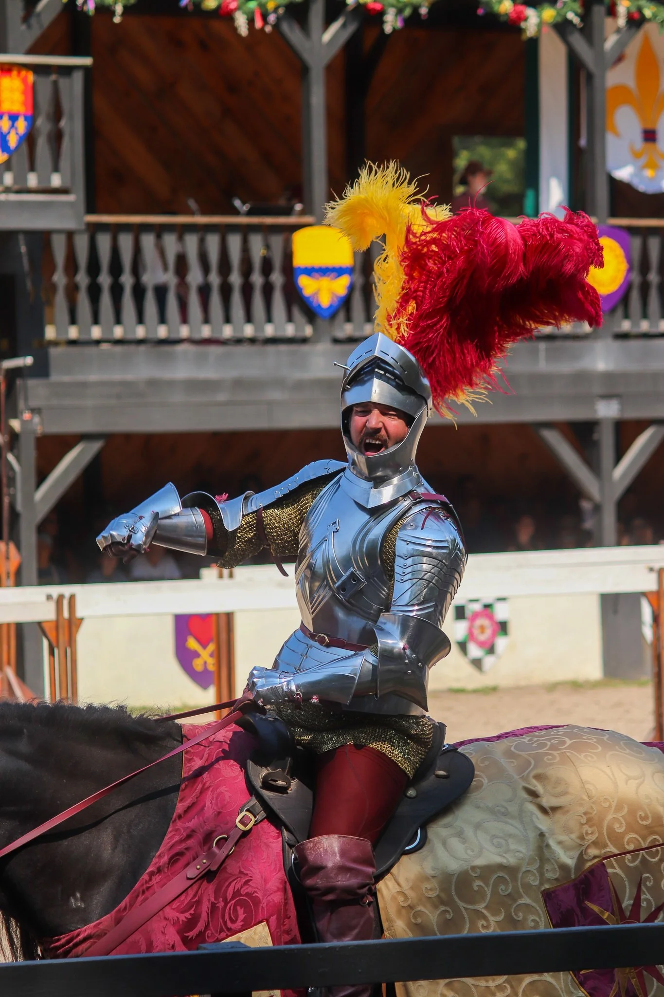 A man dressed in full medieval armor riding a horse at a renaissance fair or medieval reenactment event.