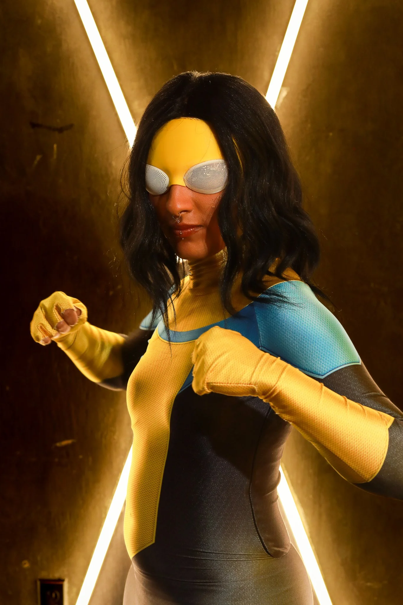 A woman in a colorful athletic suit and yellow gloves, wearing sunglasses, in a futuristic corridor with yellow lighting.