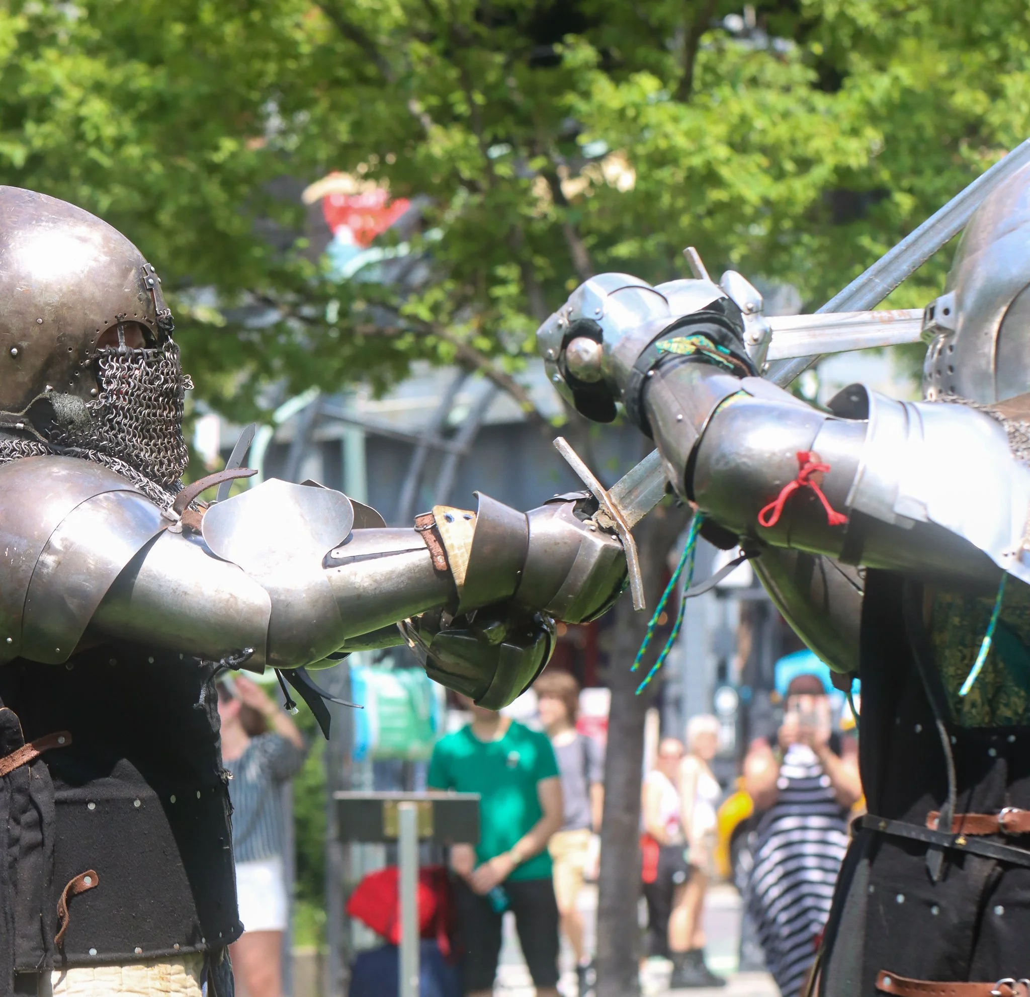 A person wearing medieval armor, including a helmet and chainmail, appears to be grilling or working near a barbecue, with a lush green park and people in the background.