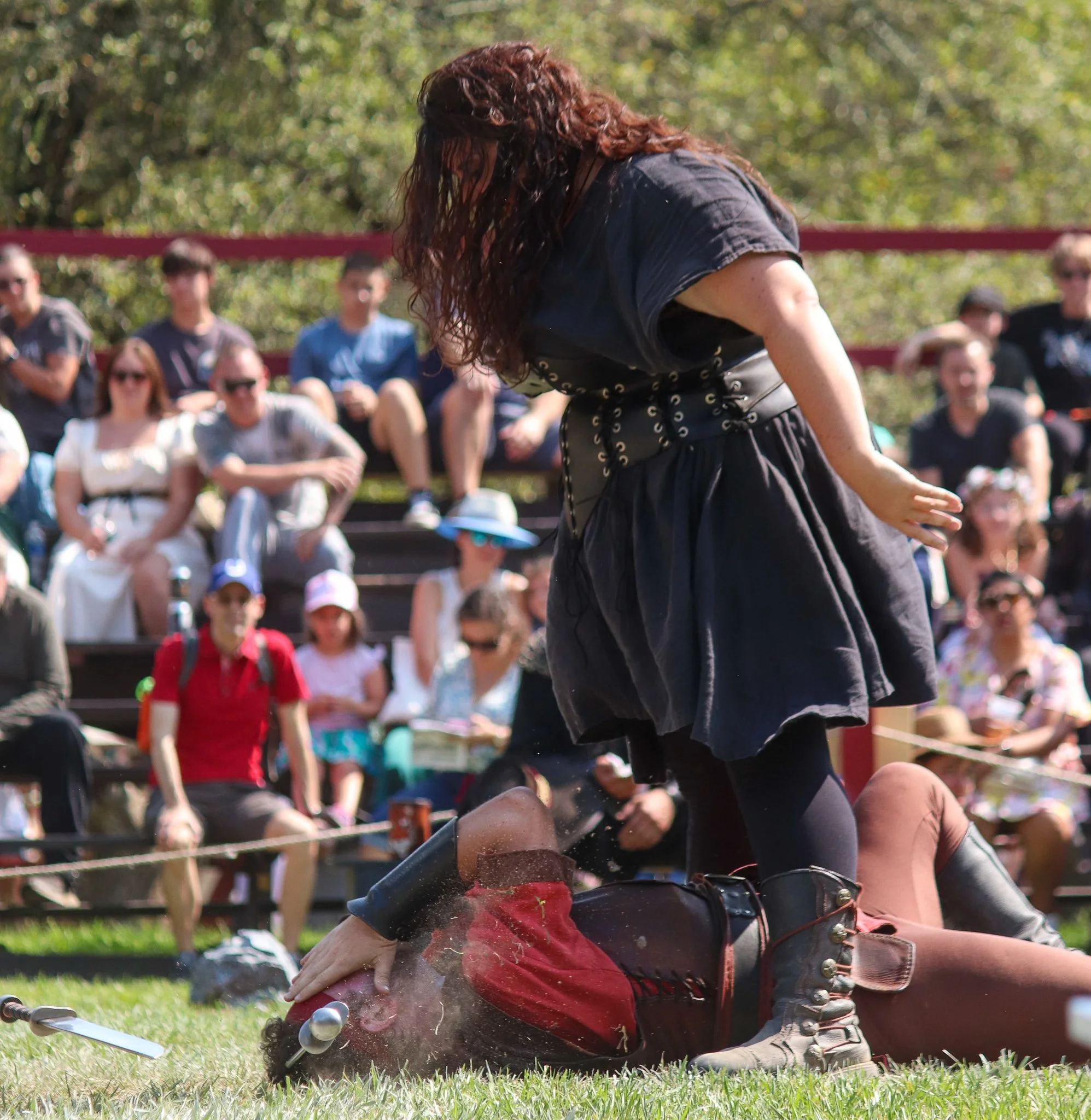 A woman with curly hair and a black dress fallen over on a golf course, surrounded by a group of people watching her.