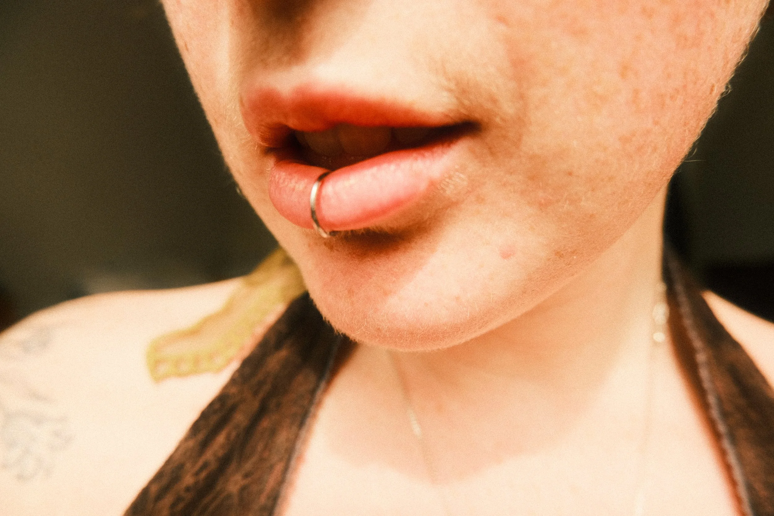 Close-up of a person's lips with a silver lip ring, partially open mouth, and braided hair.