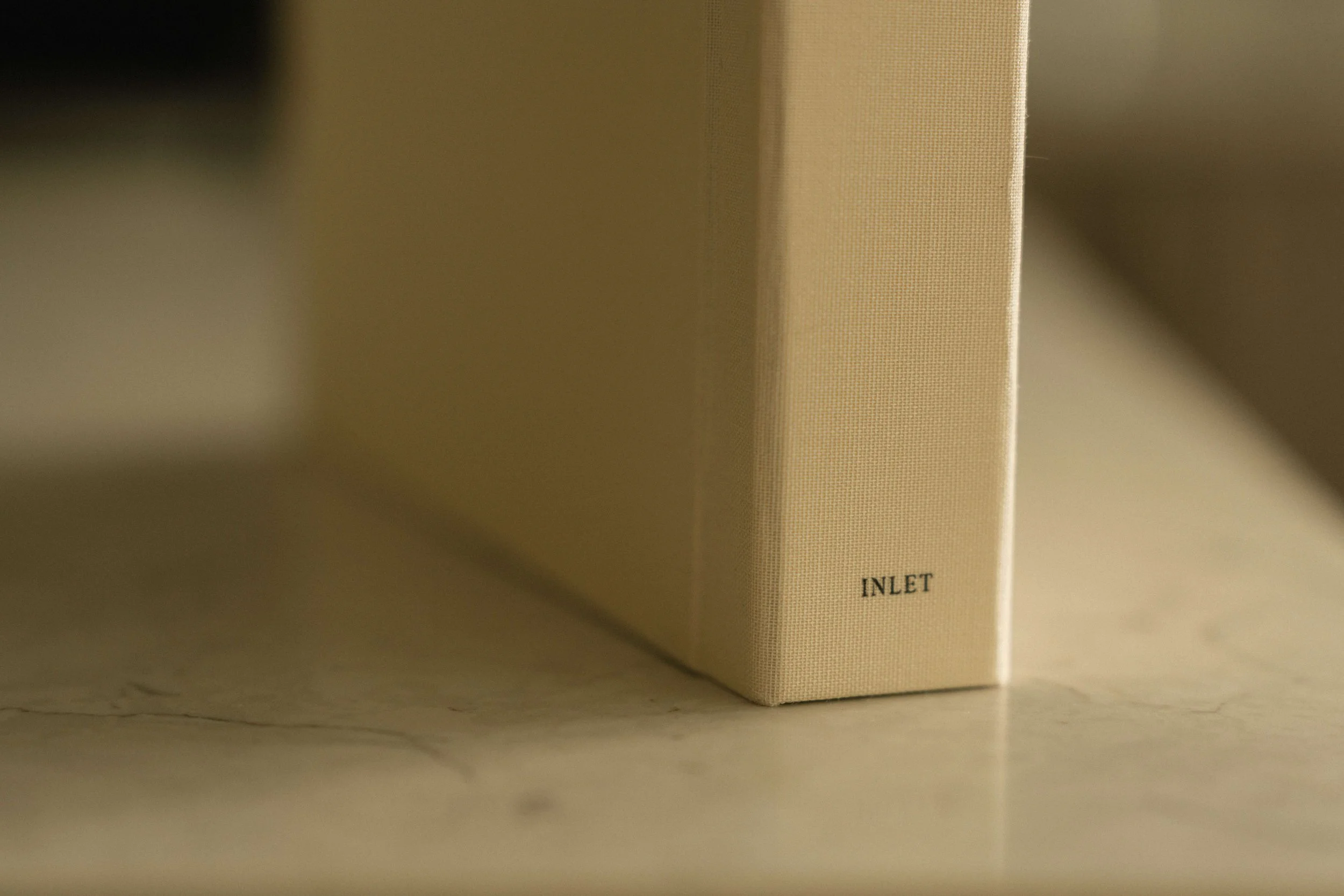 Close-up of a beige book with the word "INLET" visible on the spine, placed on a light-colored surface.