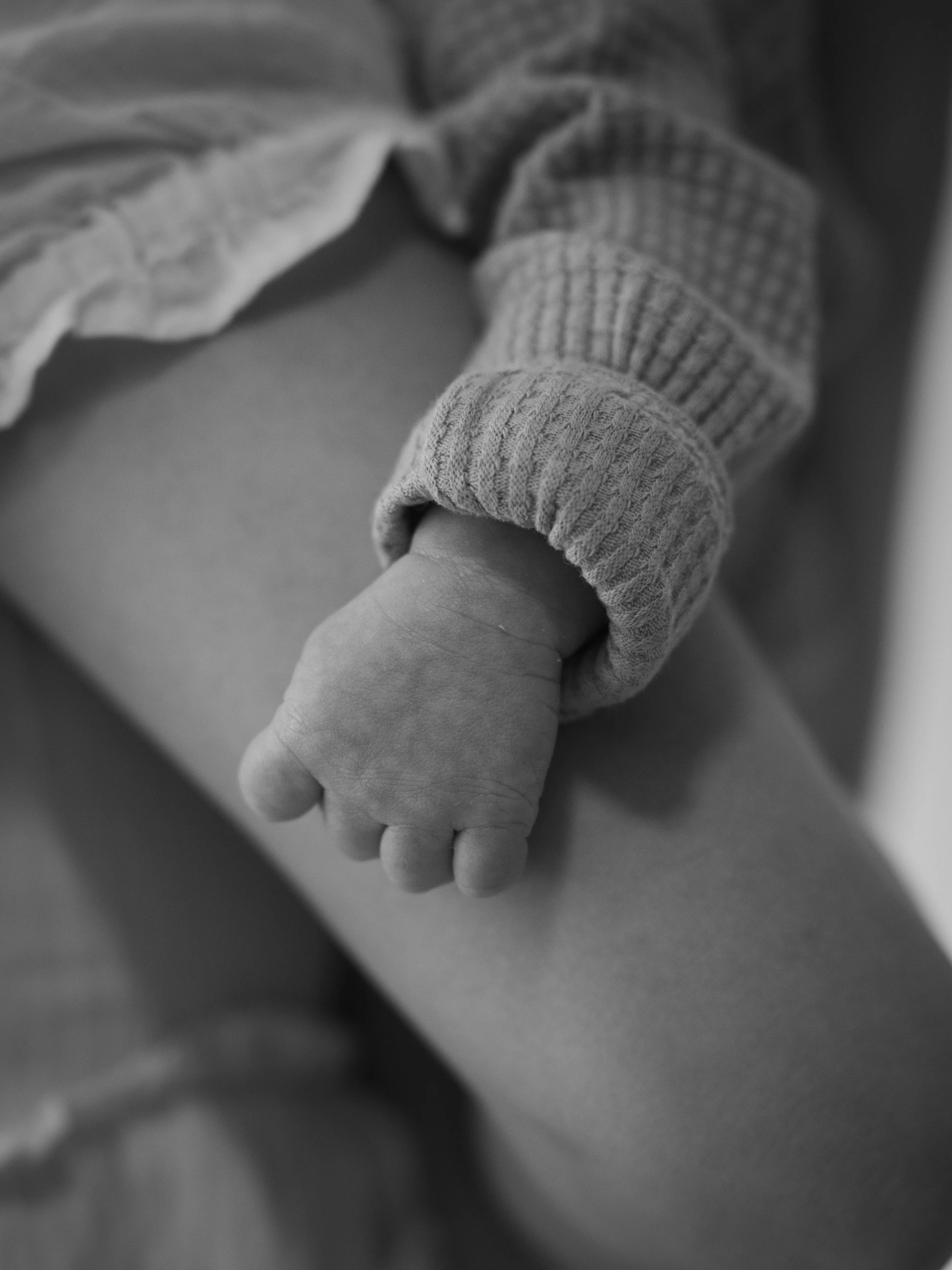 Close-up of a person's hand holding a child's hand, both wearing long-sleeved clothing, in black and white.