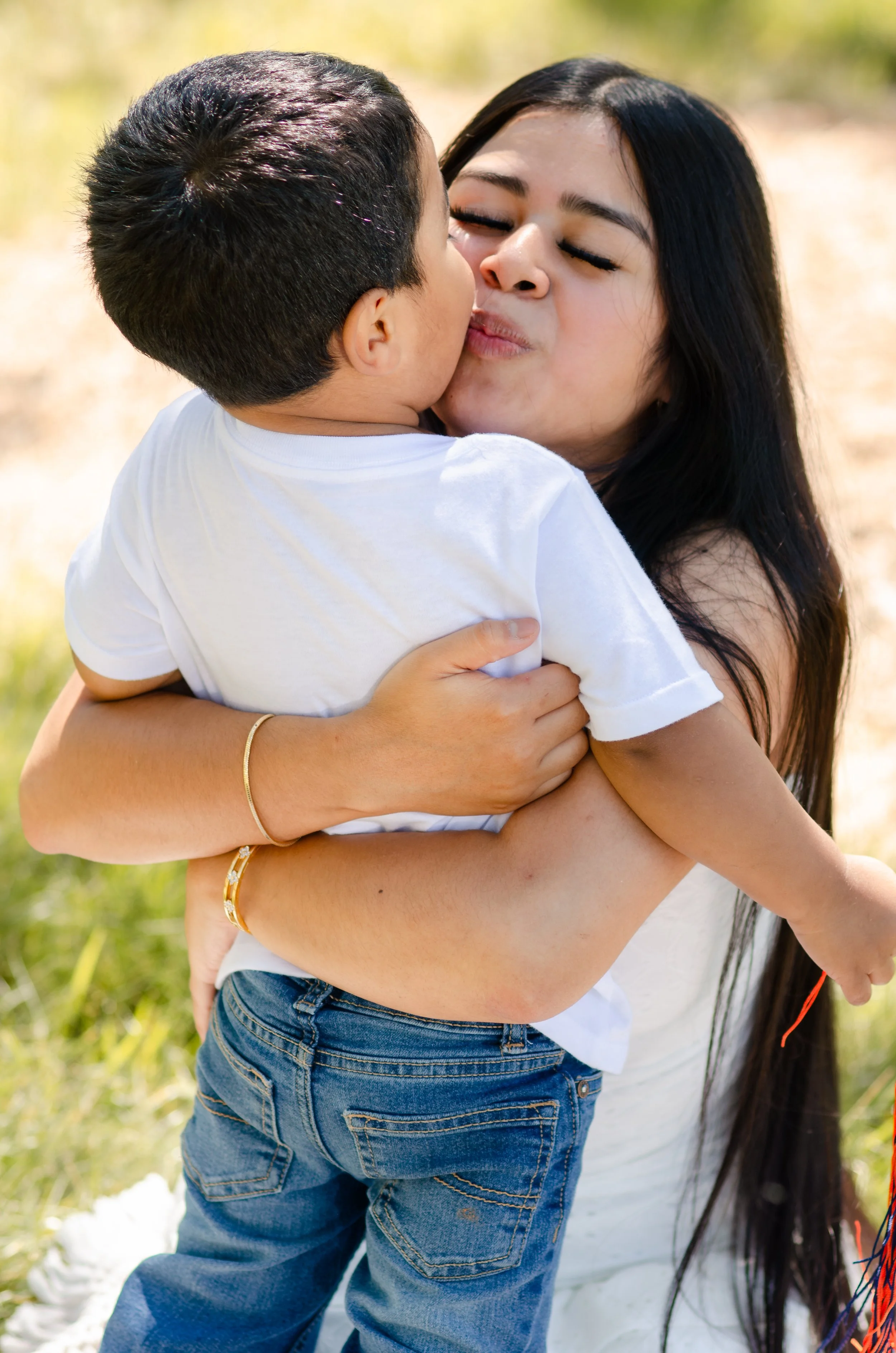  Natural mommy and me session with a mother kissing her baby boy while surrounded by soft greenery 