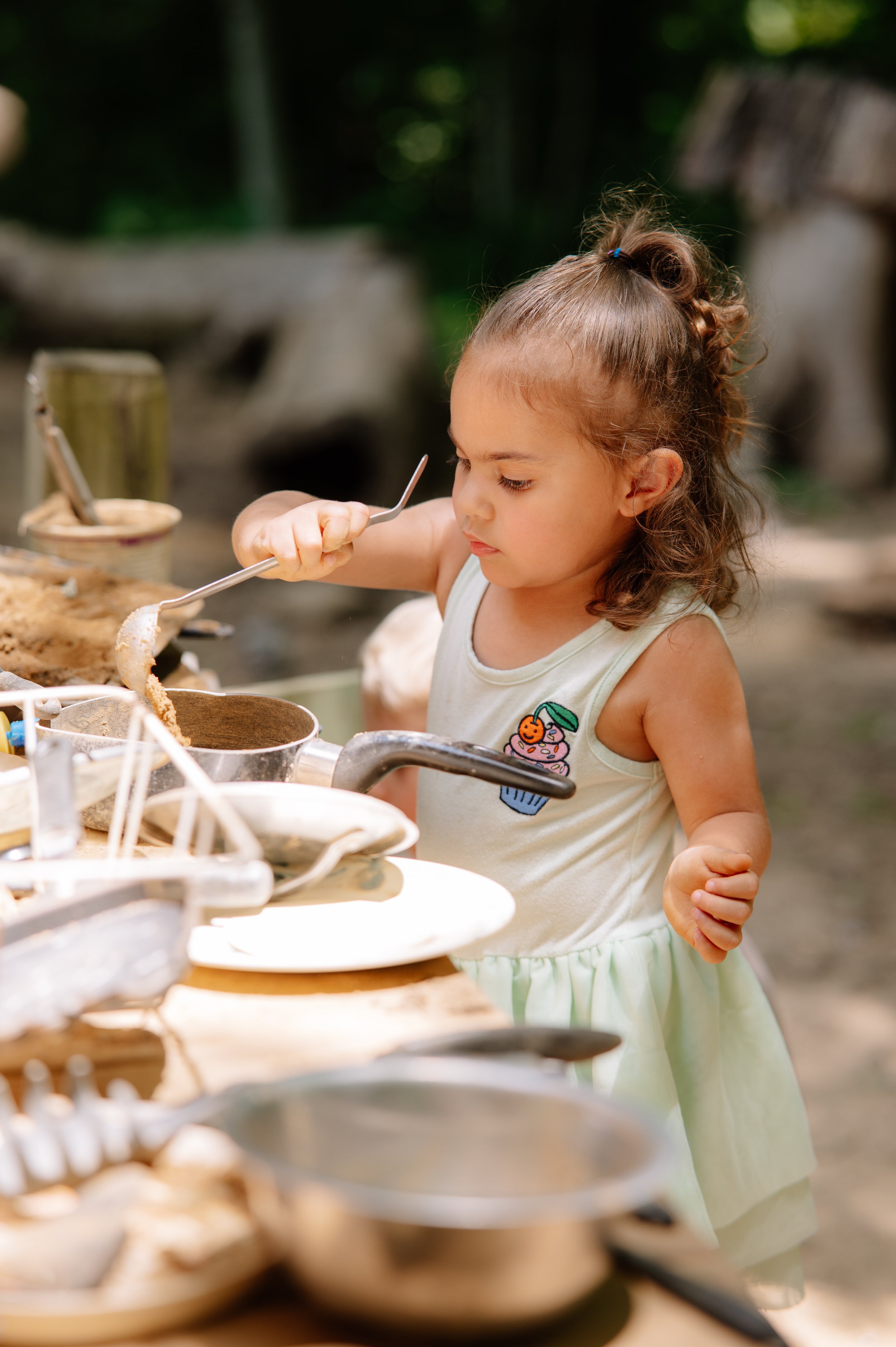 Natural childhood portrait of a girl cooking in a handmade mud kitchen surrounded by trees in townsend tn