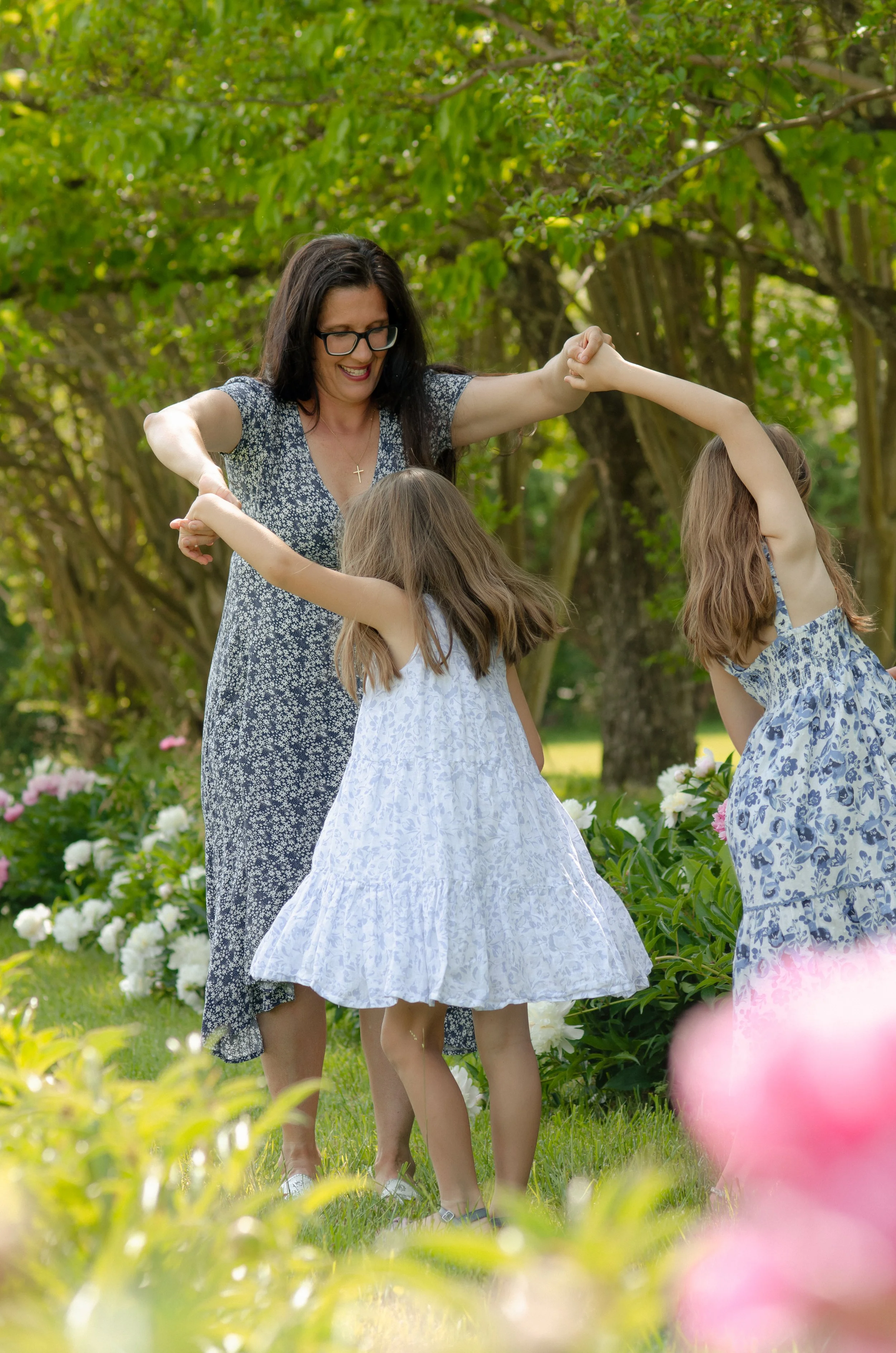 Outdoor mommy and me playful session with candid interaction in a Knoxville garden with trees and white and pink flowers.