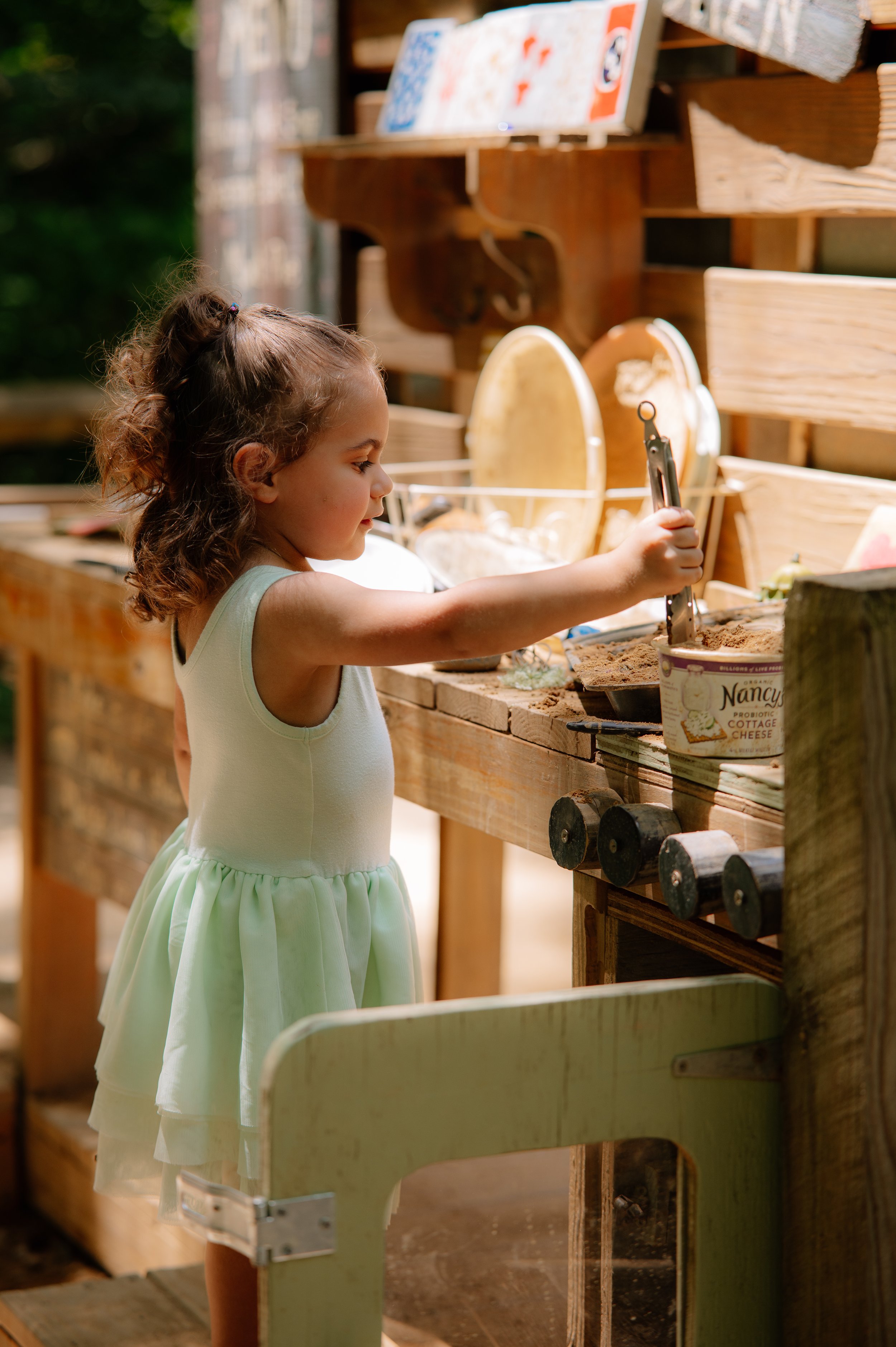 Little girl playing in a mud kitchen during an outdoor childhood photography session in Maryville TN