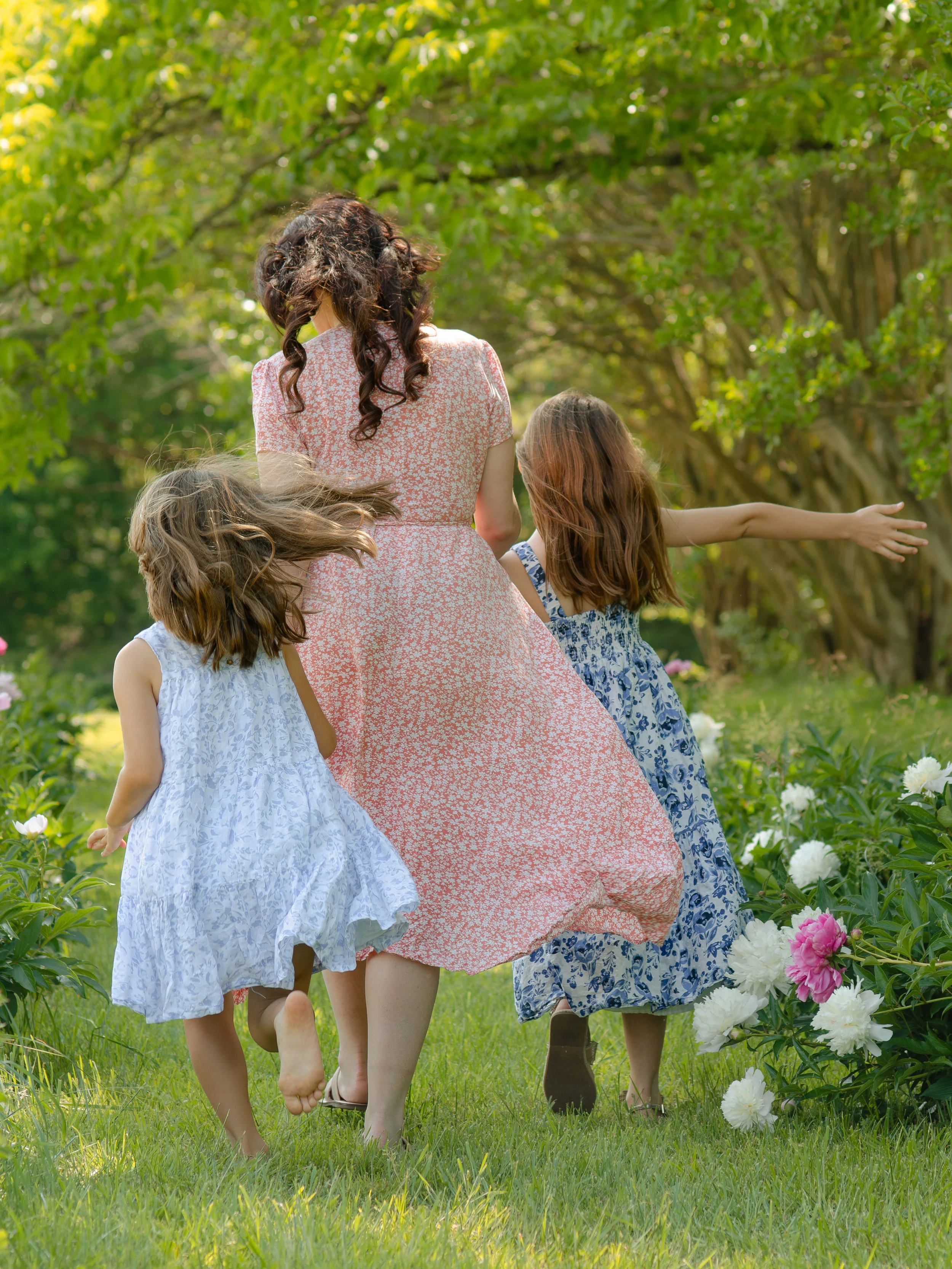 Knoxville mommy and me session capturing candid moments in a flower field walking through a garden with green trees and blooming peonies.