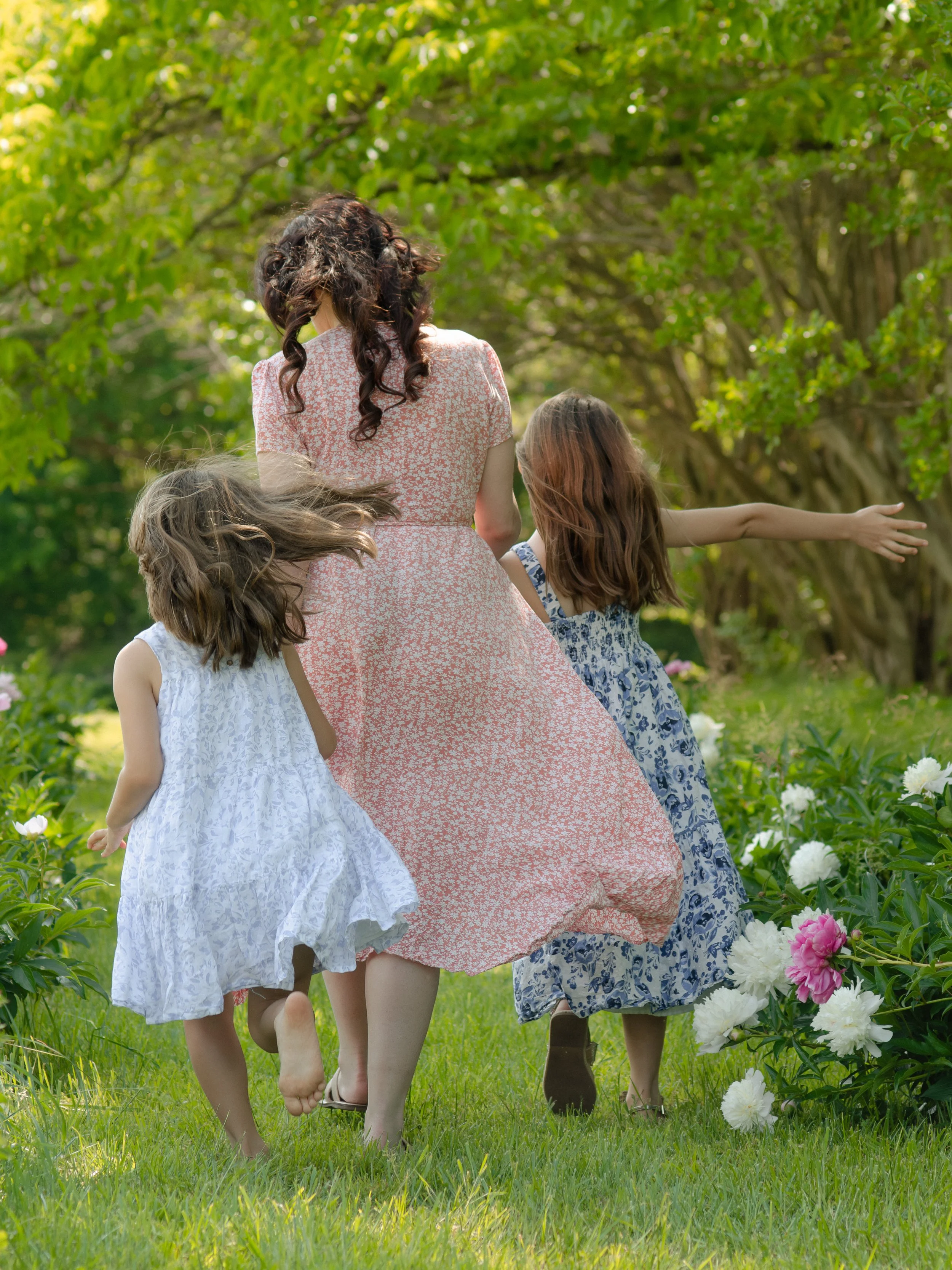Knoxville mommy and me session capturing candid moments in a flower field walking through a garden with green trees and blooming peonies.