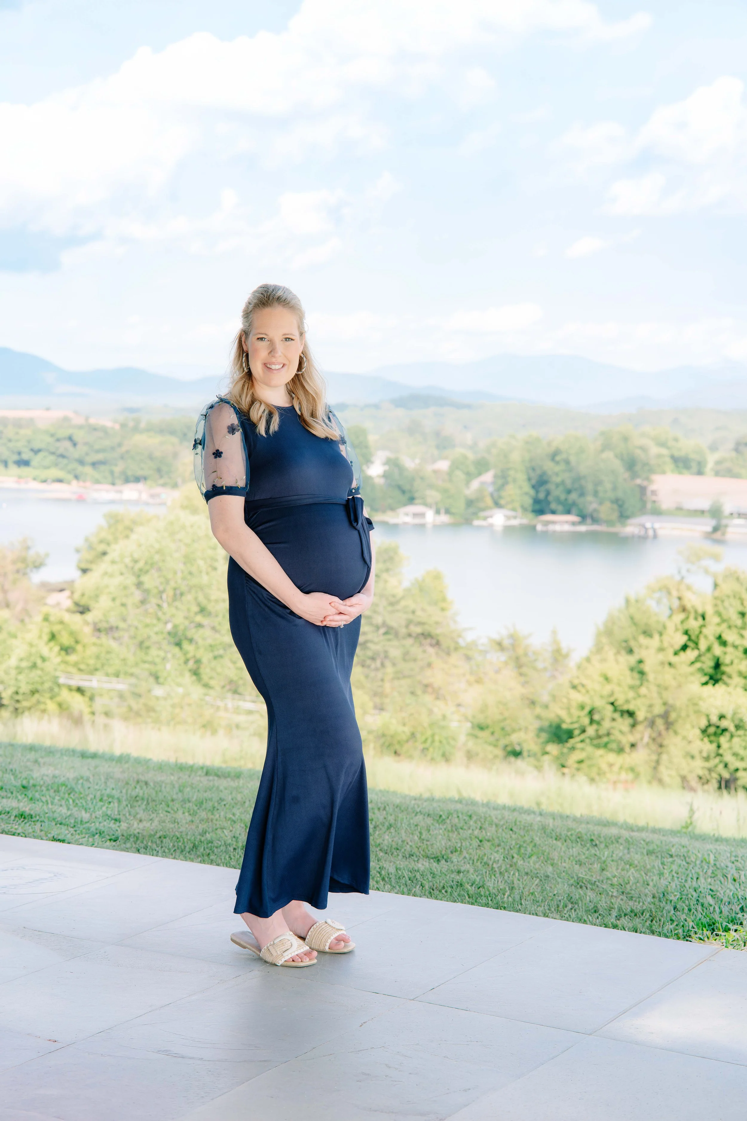 Expecting mother smiling and cradling her baby bump with a mountain lake view in the background, Vonore maternity photography