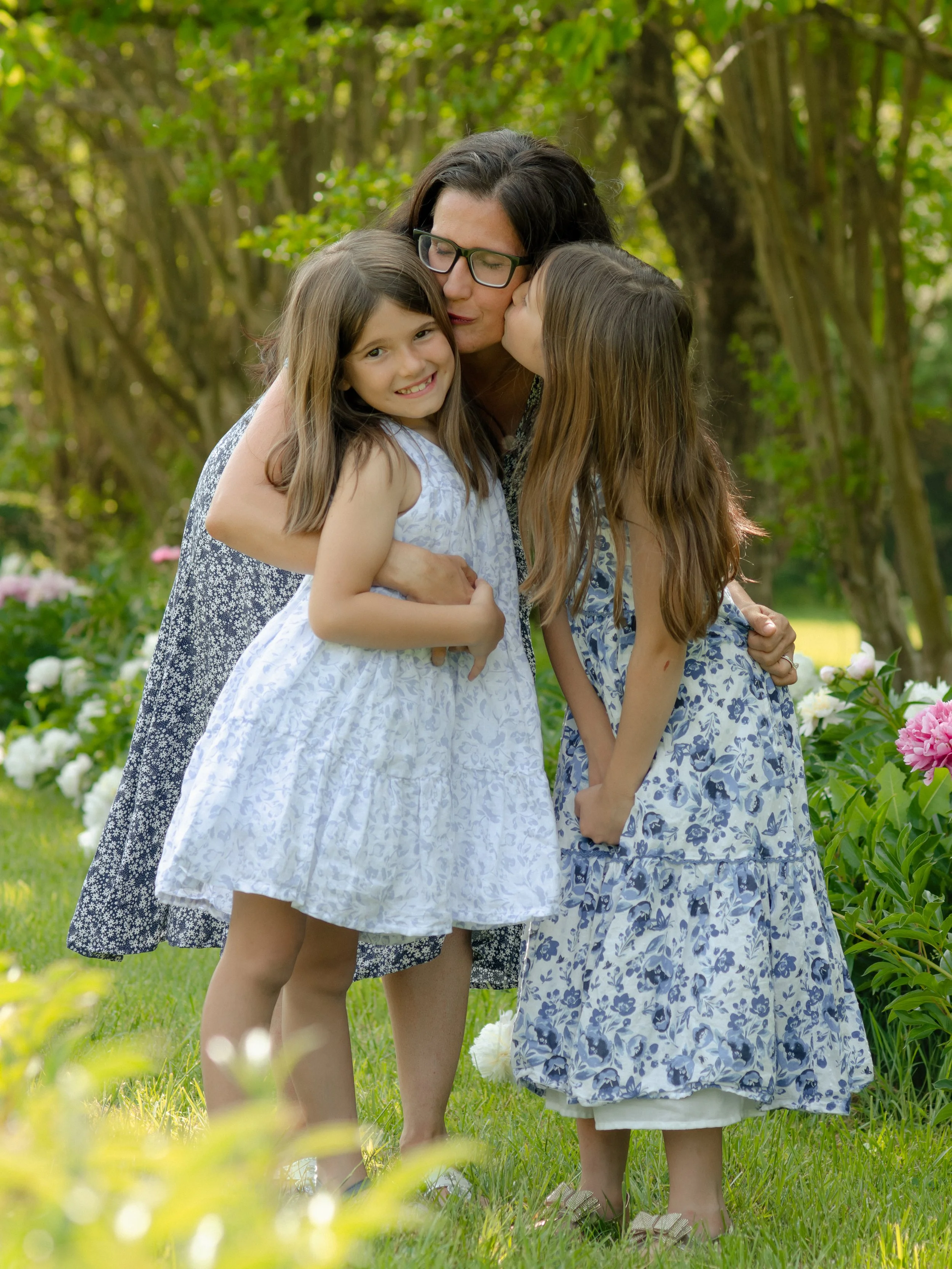 Knoxville mommy and me session with mom and daughters in a soft, airy outdoors in a garden surrounded by green trees and colorful flowers.