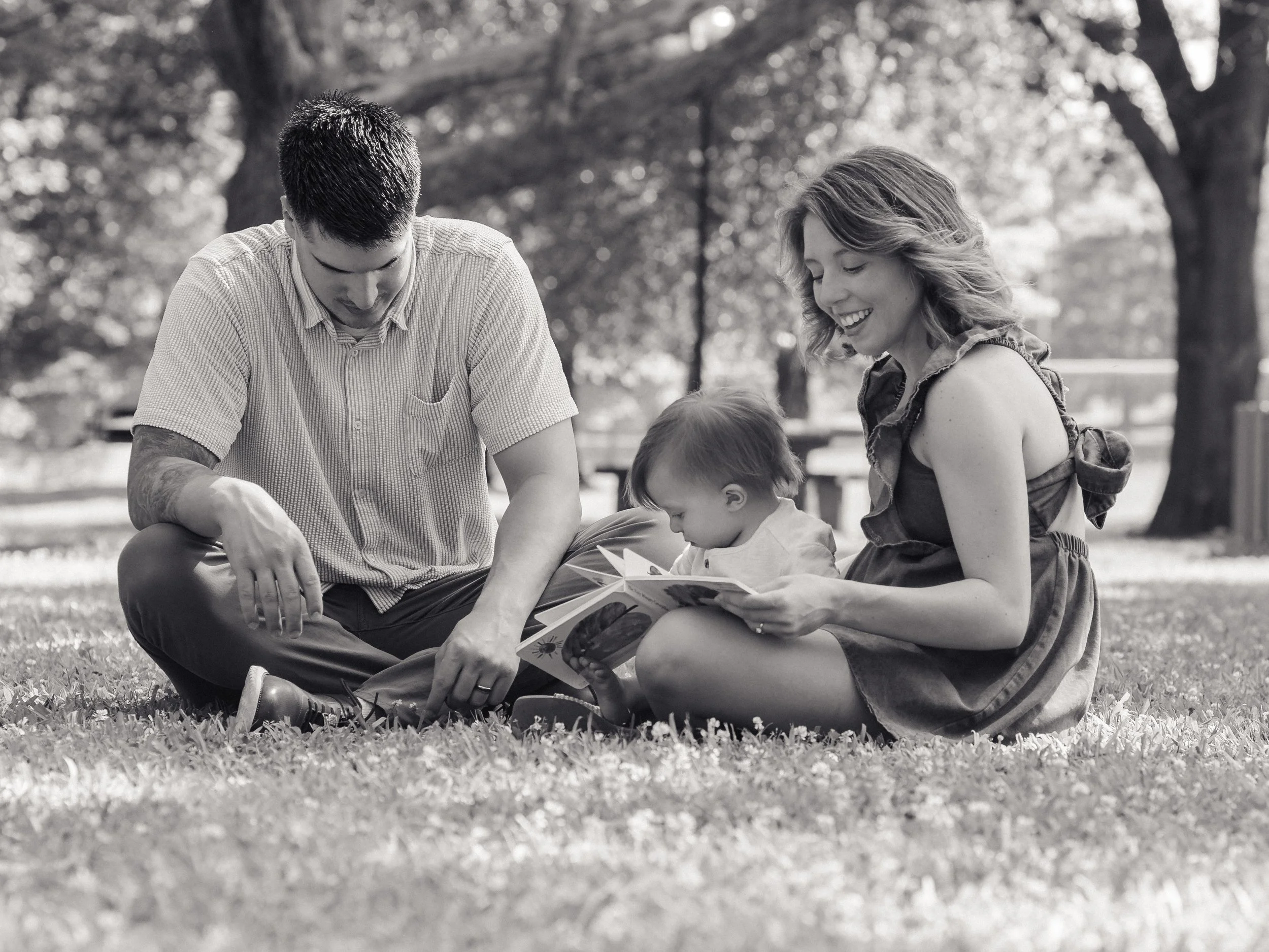 Toddler cuddling with his parents during a natural family photography session in Maryville at Sandy Springs Park while mom reads a book