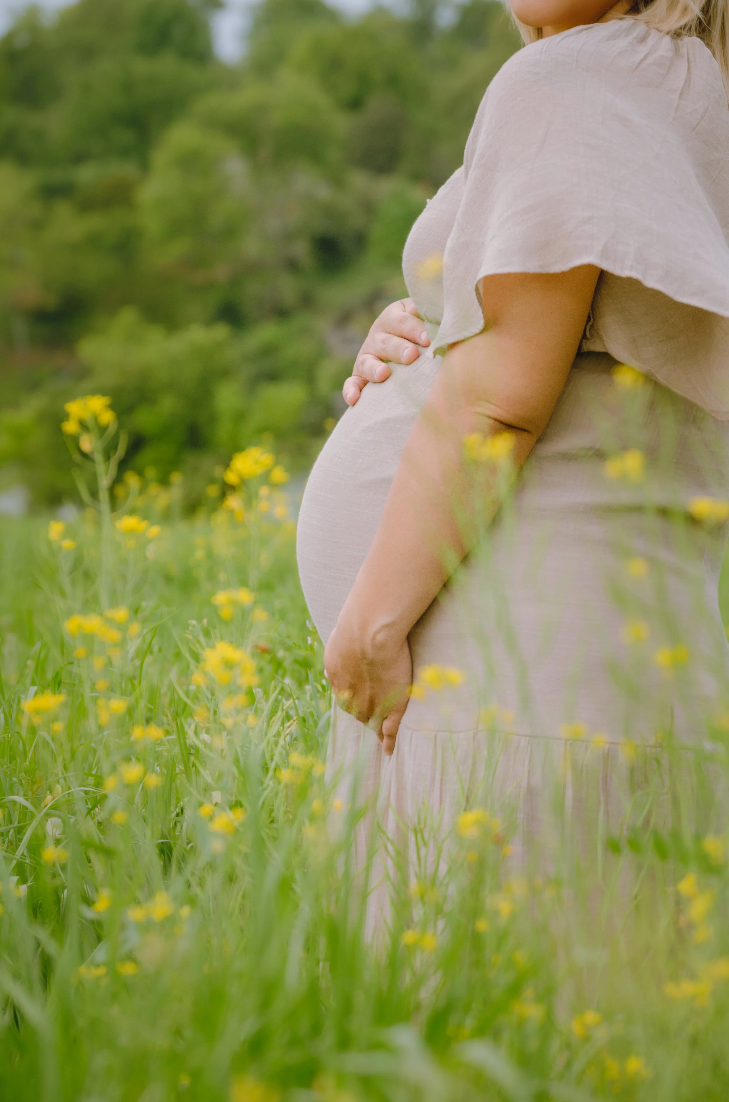Outdoor maternity session in Knoxville with natural, unposed moments,  standing outdoors in a field of yellow flowers, with trees in the background