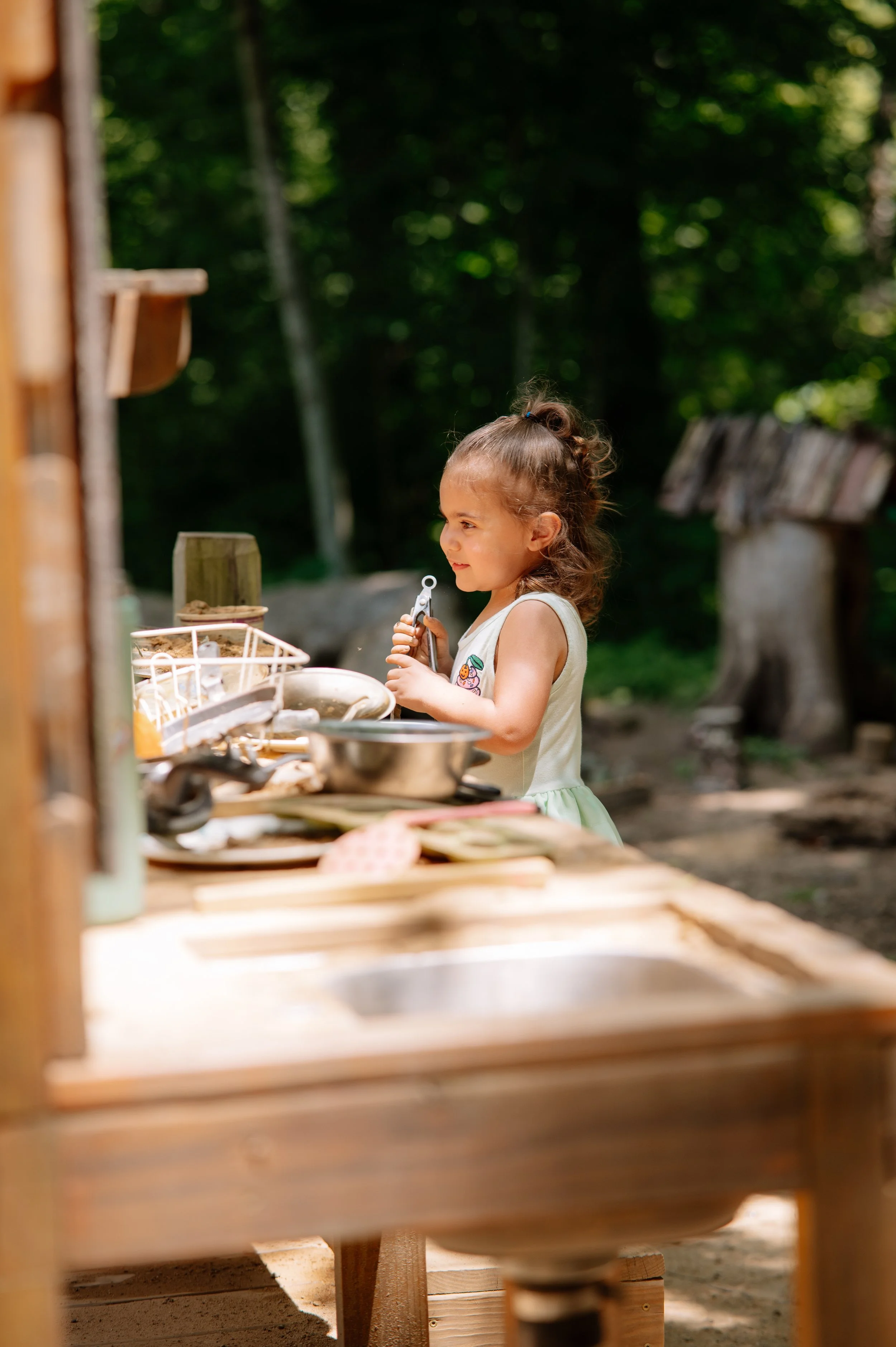 Maryville child photographer capturing a little girl playing outdoors in a woodland mud kitchen