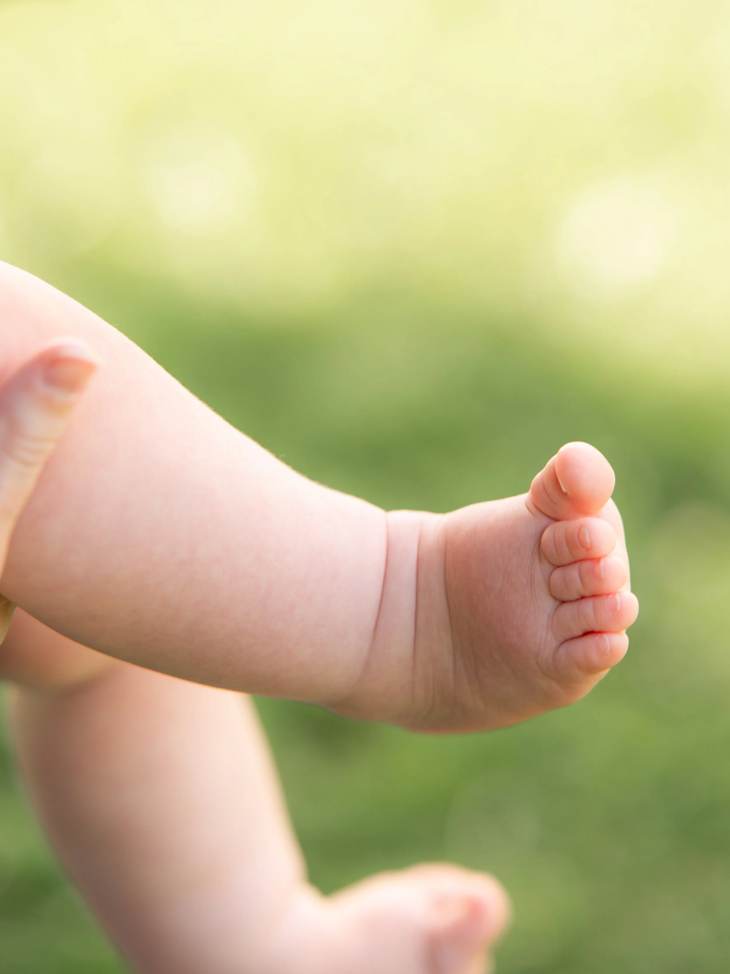 Close-up of a baby's hand with fingers extended, outdoors with blurred green background.