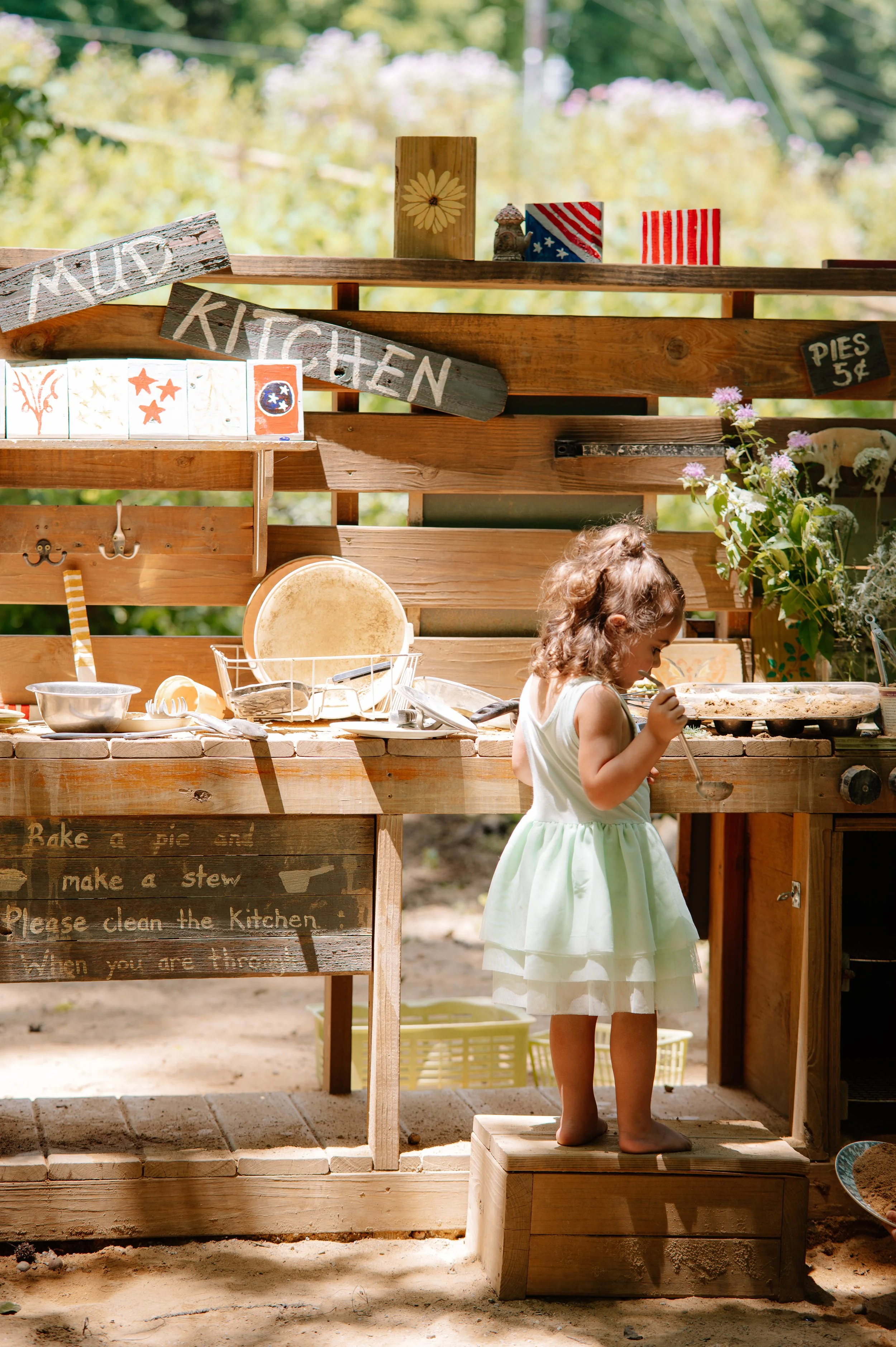Little girl mixing mud and leaves in a woodland play kitchen during a family photography session