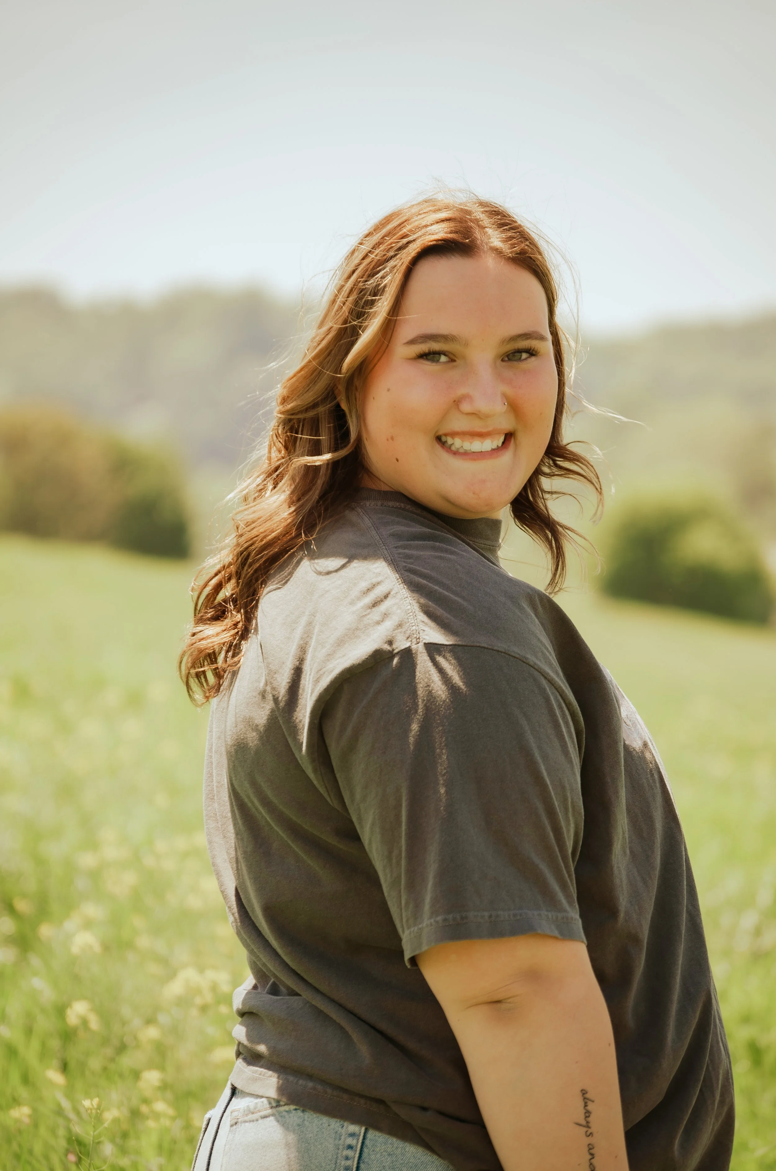 Smiling young woman with brown hair outdoors in a green field on a sunny day.