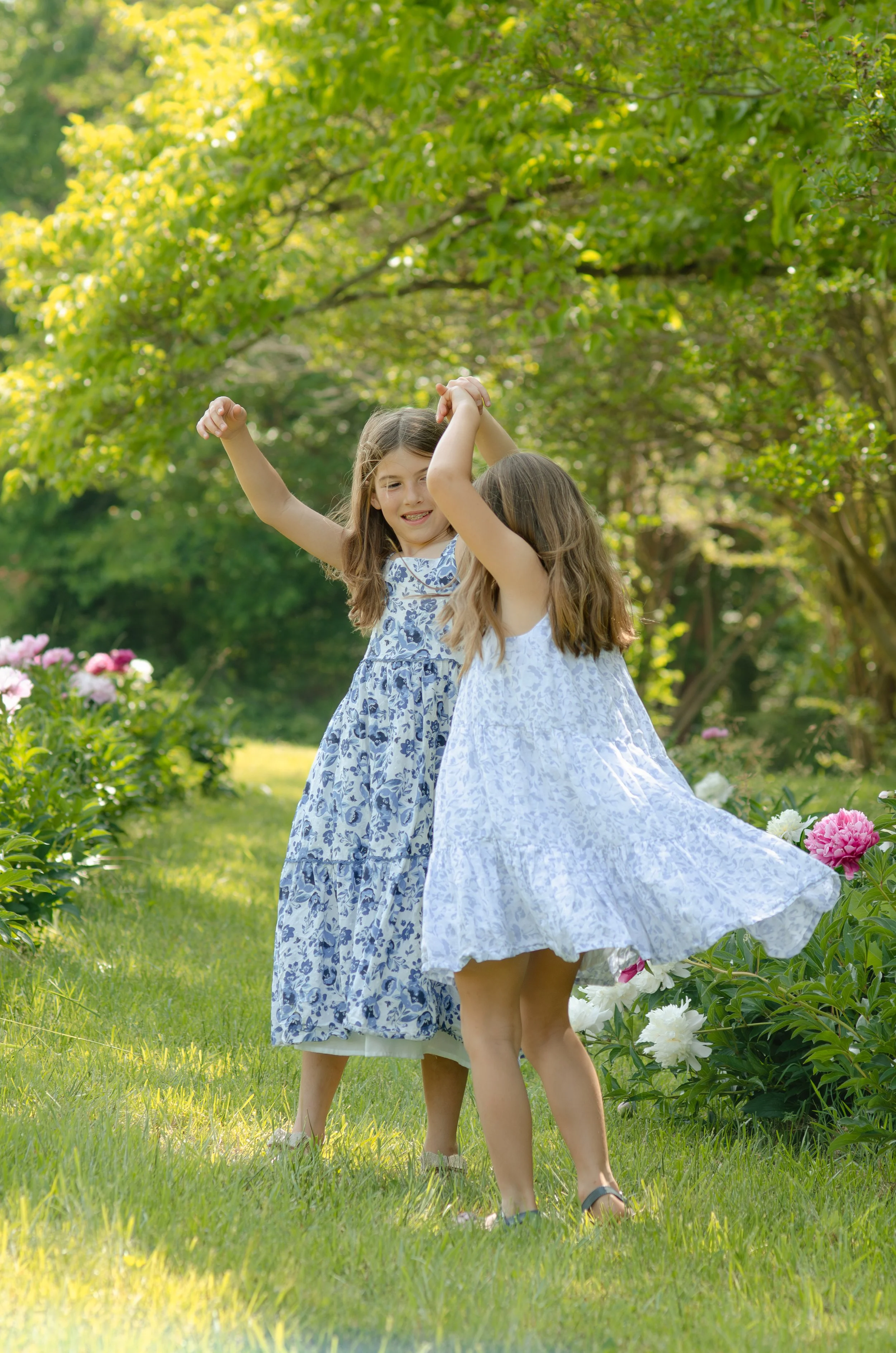 Knoxville photosession with two sisters playing and dancing together outdoors in a beautiful garden with flowering bushes and trees on a sunny day.