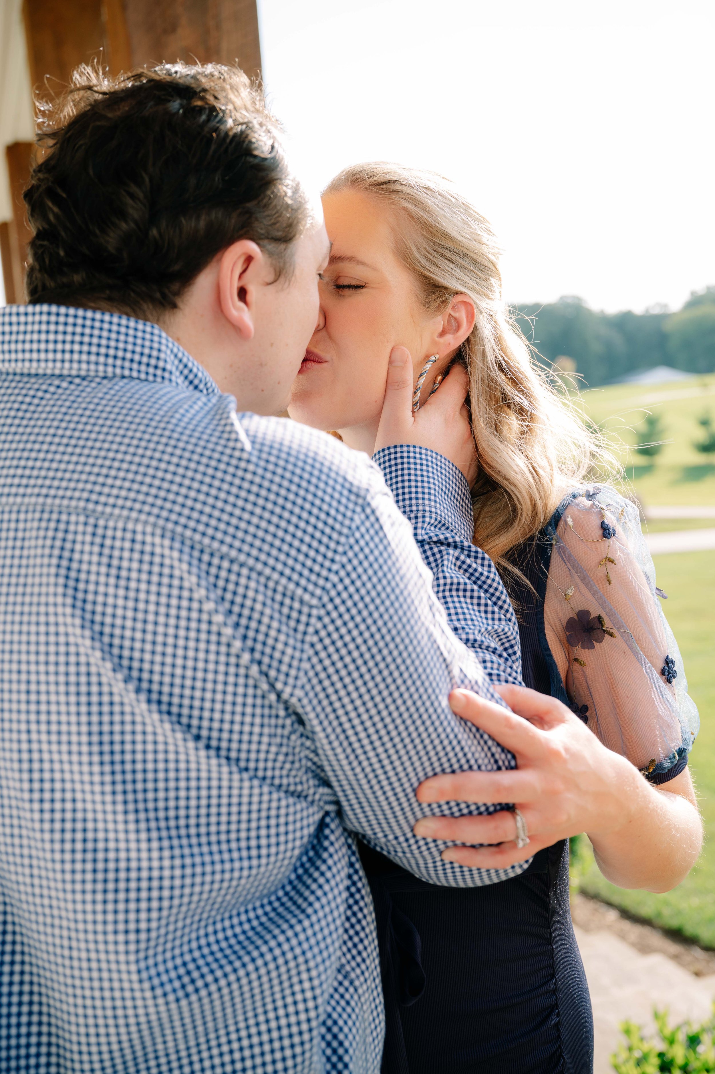 Husband kissing his pregnant wife on a sunlit farmhouse porch during a Maryville maternity session