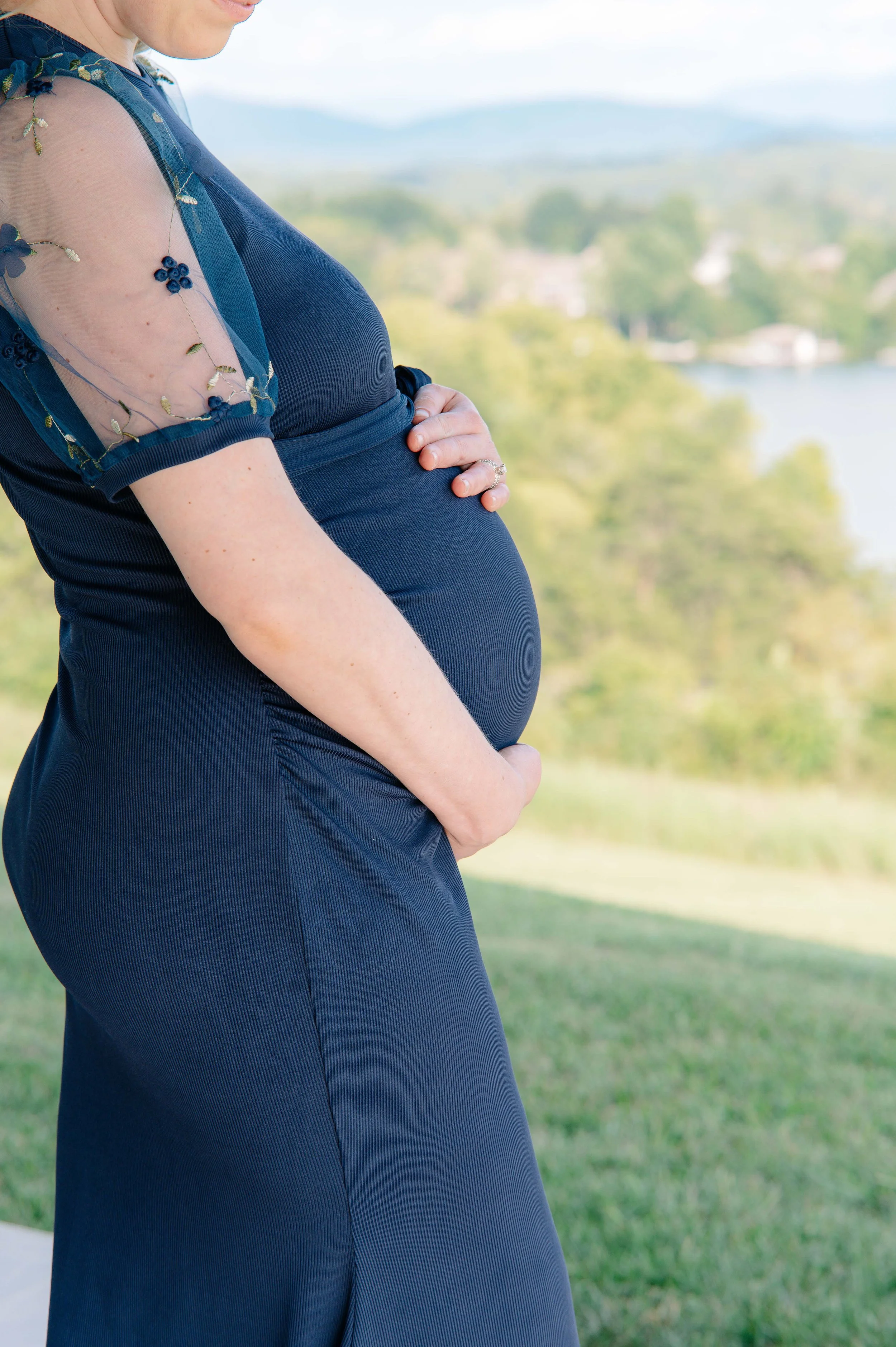 Close-up of a pregnant belly in a navy dress with lake and Smoky Mountains view, Vonore TN maternity session