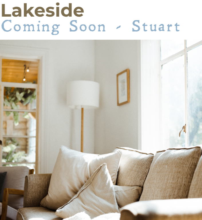 Cozy living room with a beige sofa, cream pillows, a white lamp, and large windows letting in natural light.