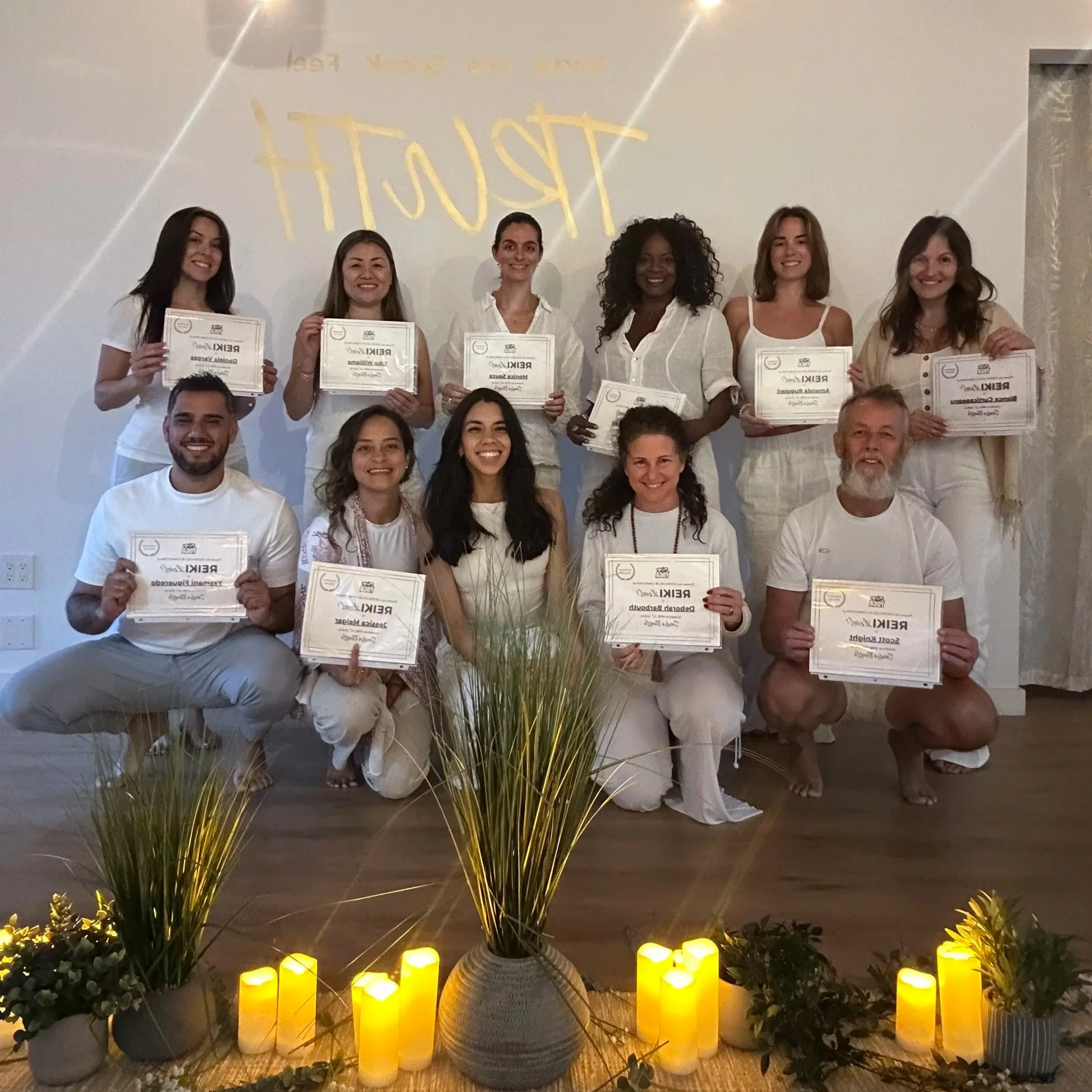 Group of six women and two men holding certificates in a celebration or awards event, with candles and plants as decoration.