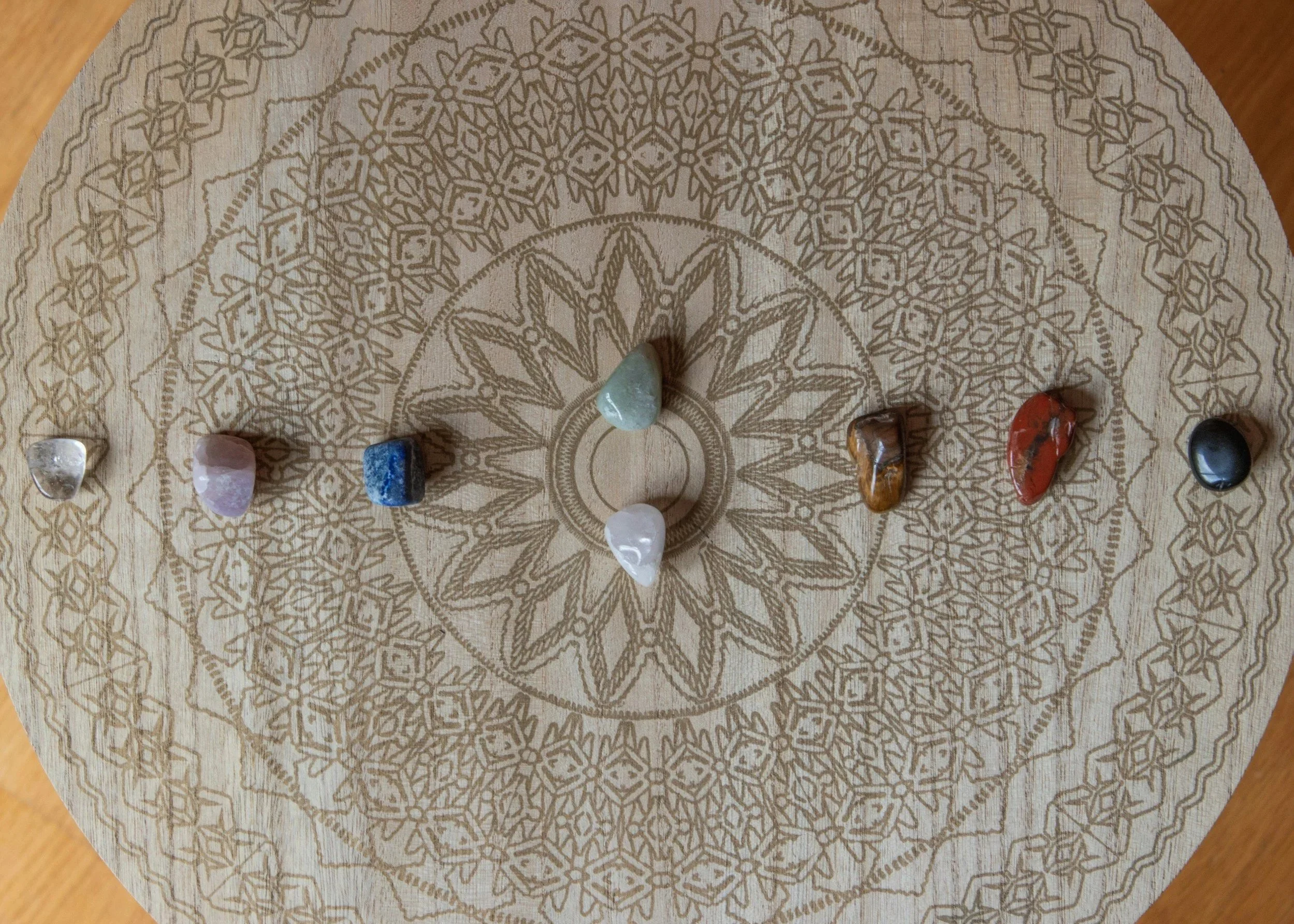A wooden board with an intricate geometric pattern engraved on it, featuring a variety of semi-precious stones placed on the pattern.