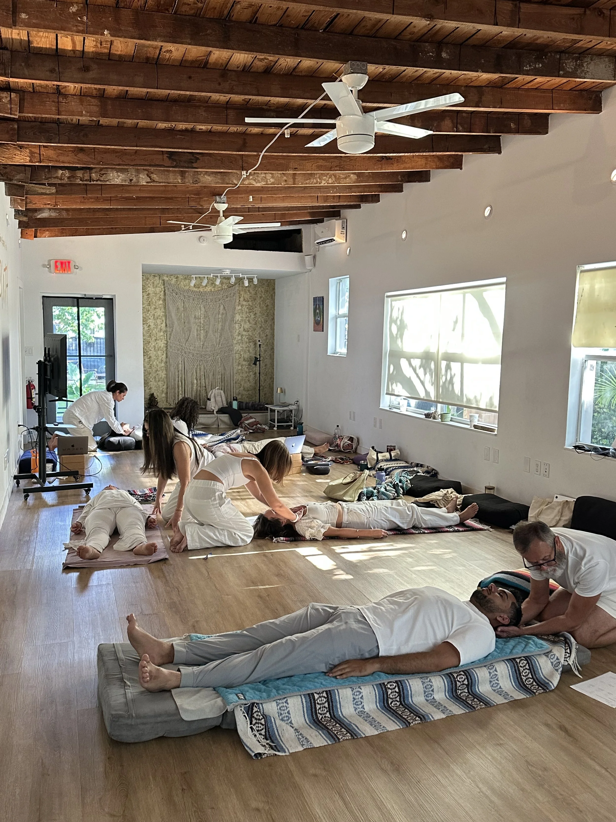 People participating in a mindful meditation session in a spacious room with wooden ceiling beams and large windows.