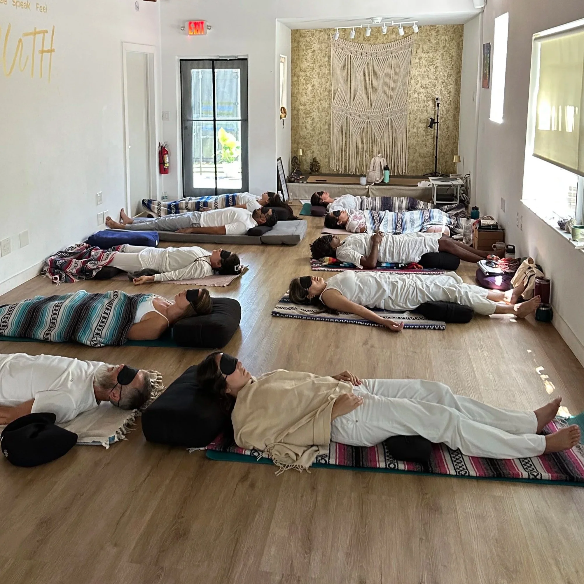 People lying on yoga mats with eyes closed in a peaceful room during a meditation or yoga session.