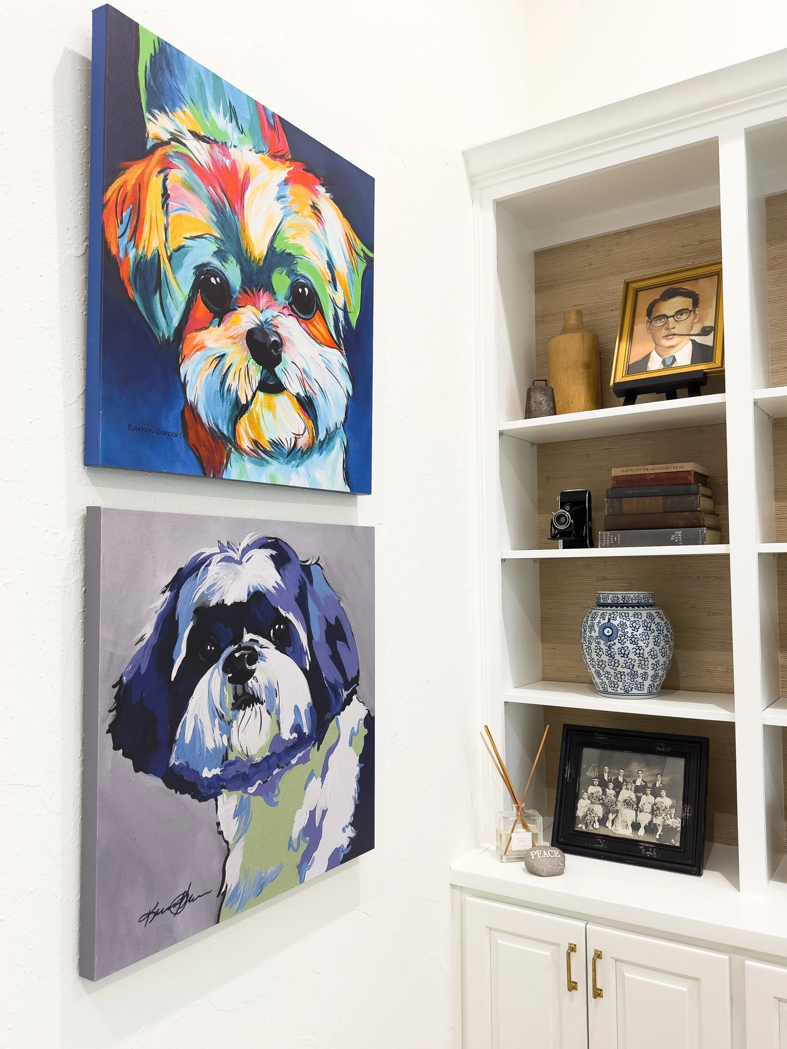 Colorful portrait of a small dog next to a black and white traditional dog picture on a white wall and a corner white shelf with decorative items.
