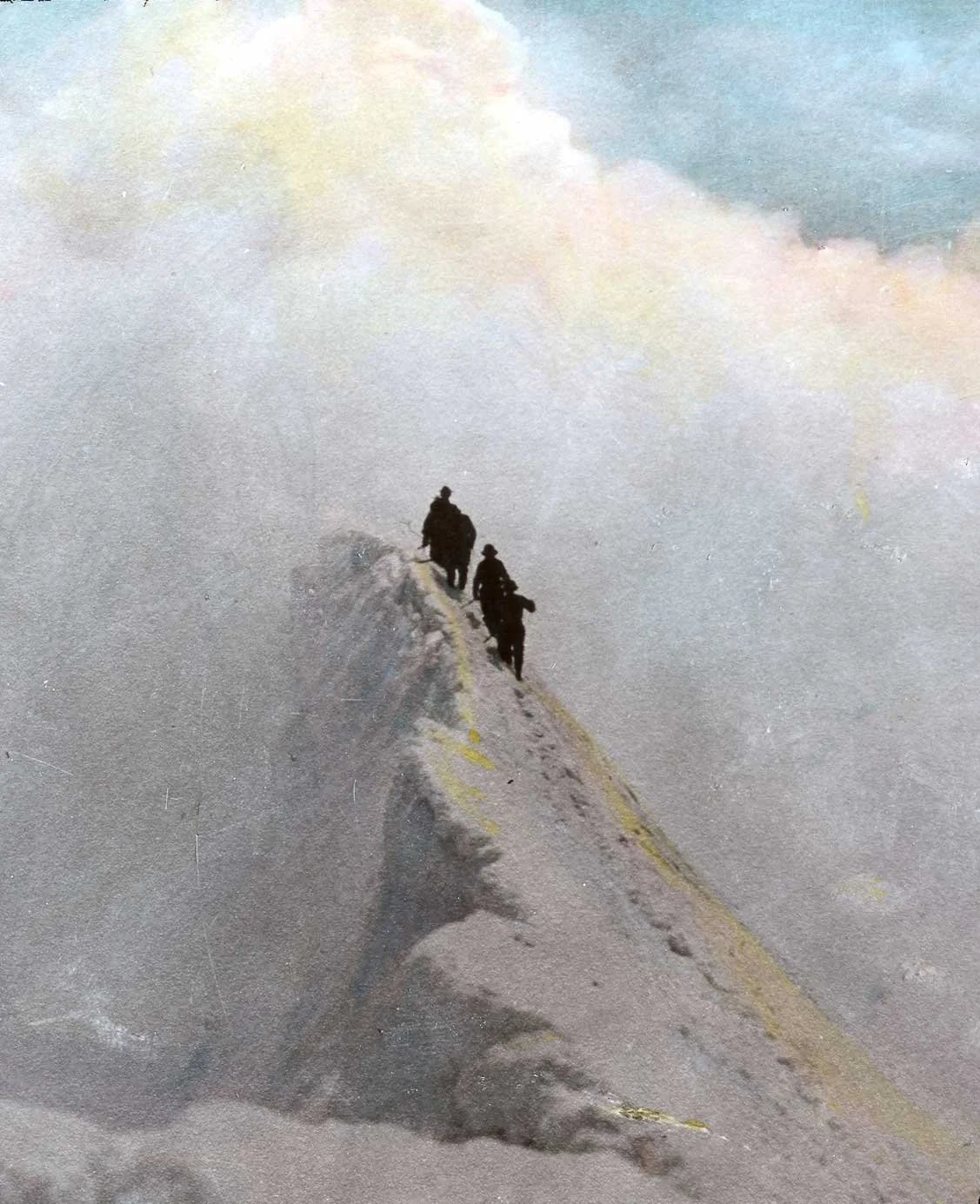 Two climbers walk along a narrow snowy ridge beneath colorful clouds on a high alpine peak