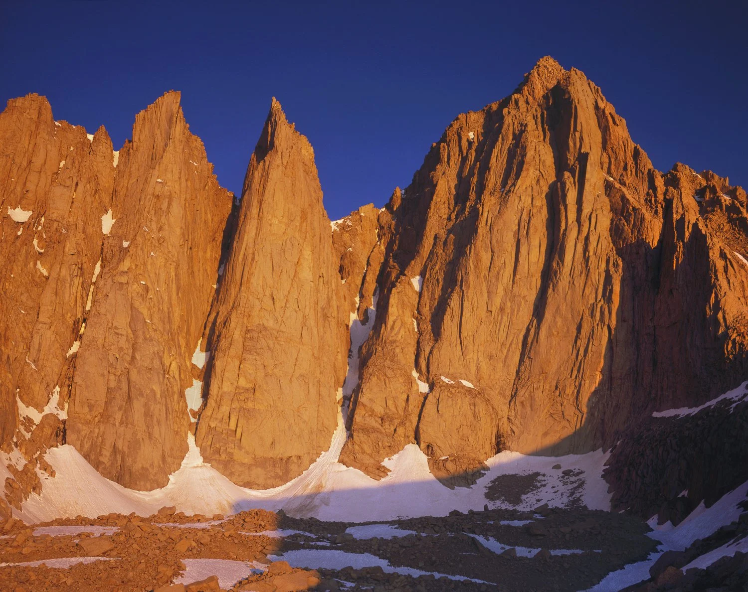 Sunlit granite spires and cliffs at sunrise with patches of snow on the East face of Mt. Whitney