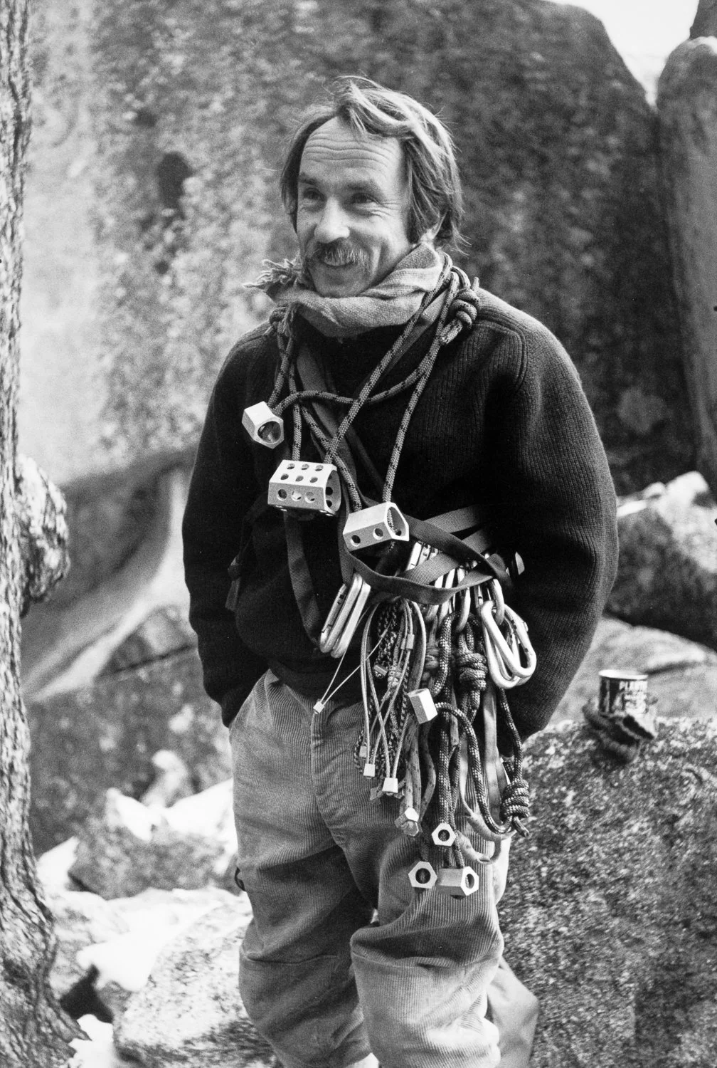 Climber at Yosemite wearing a sweater and rack of nuts and carabiners, standing among large granite boulders