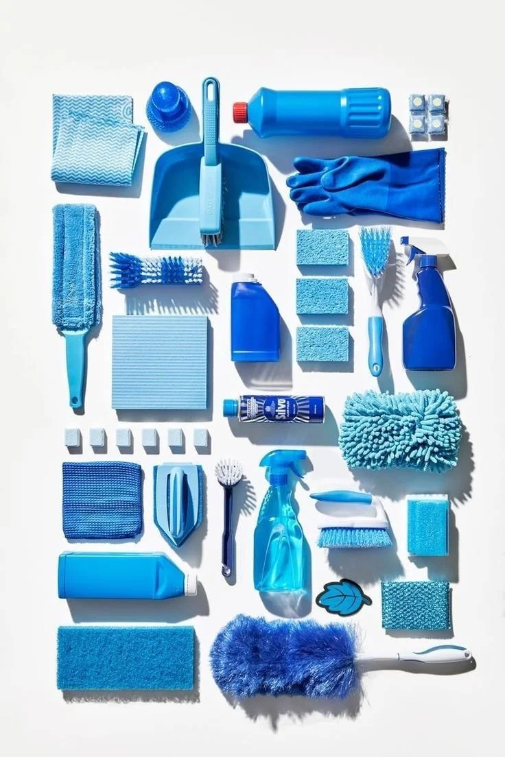Collection of blue cleaning supplies including spray bottles, sponges, scrub brushes, gloves, cloths, and cleaning agents arranged on a white background.