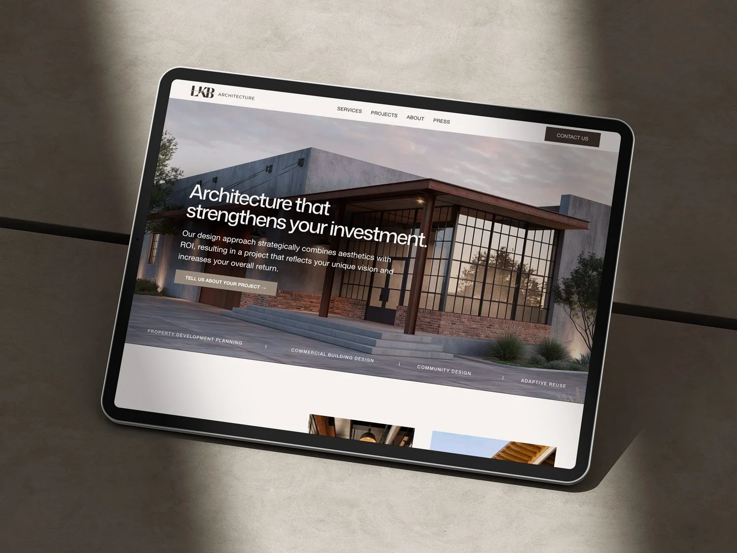 A tablet displaying a modern architecture website with a large image of a contemporary building with glass walls and a red brick base, set against a sunset sky.
