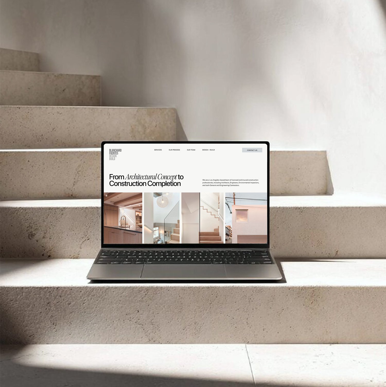 Laptop displaying a modern architecture website placed on stone stairs in a minimalist setting.