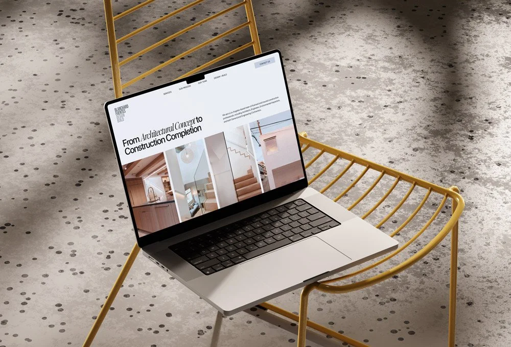 Laptop on a yellow chair displaying an architecture website, on a speckled concrete floor.