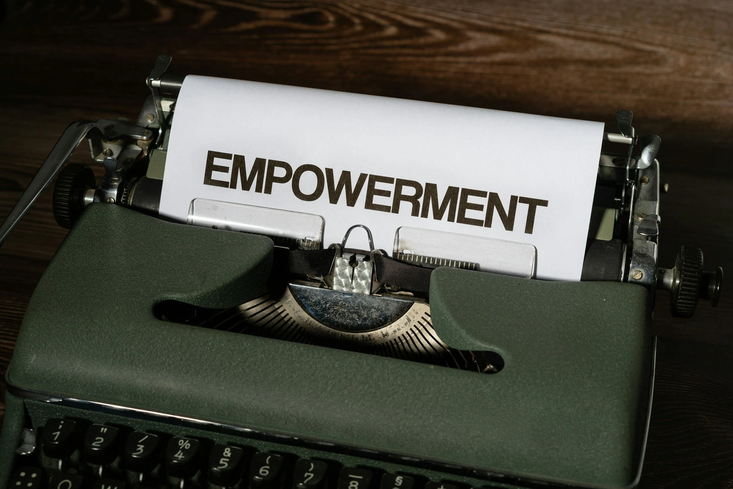 A vintage typewriter with a sheet of paper in it displaying the word 'EMPOWERMENT' in bold capital letters, placed on a dark wooden surface.