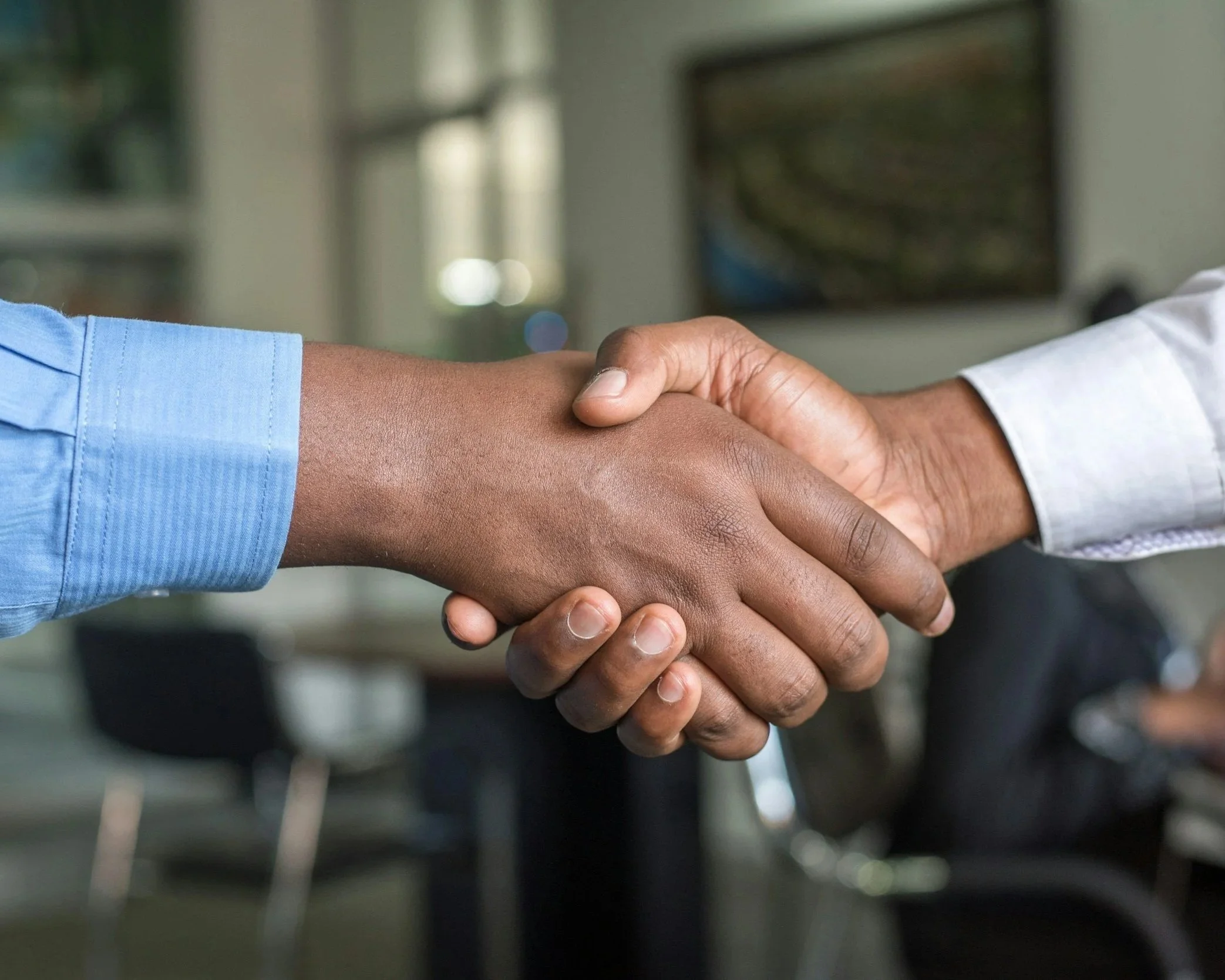 Close-up of two people shaking hands, one wearing a light blue shirt and the other wearing a white shirt.