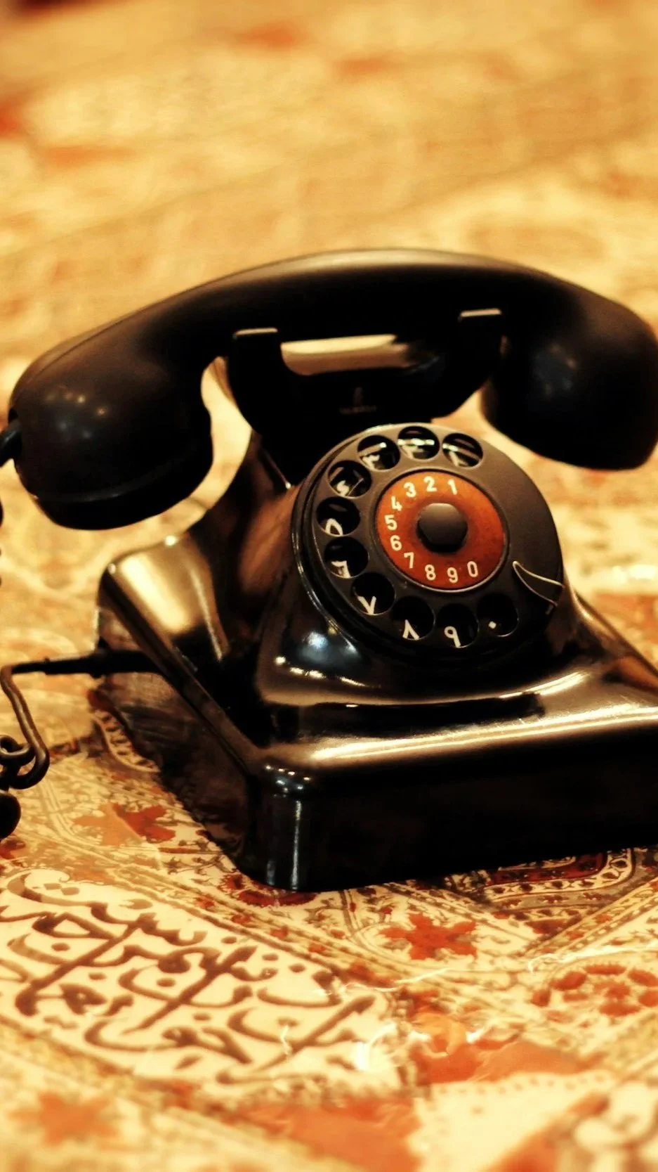 Close-up of a vintage black rotary telephone on a patterned fabric surface.