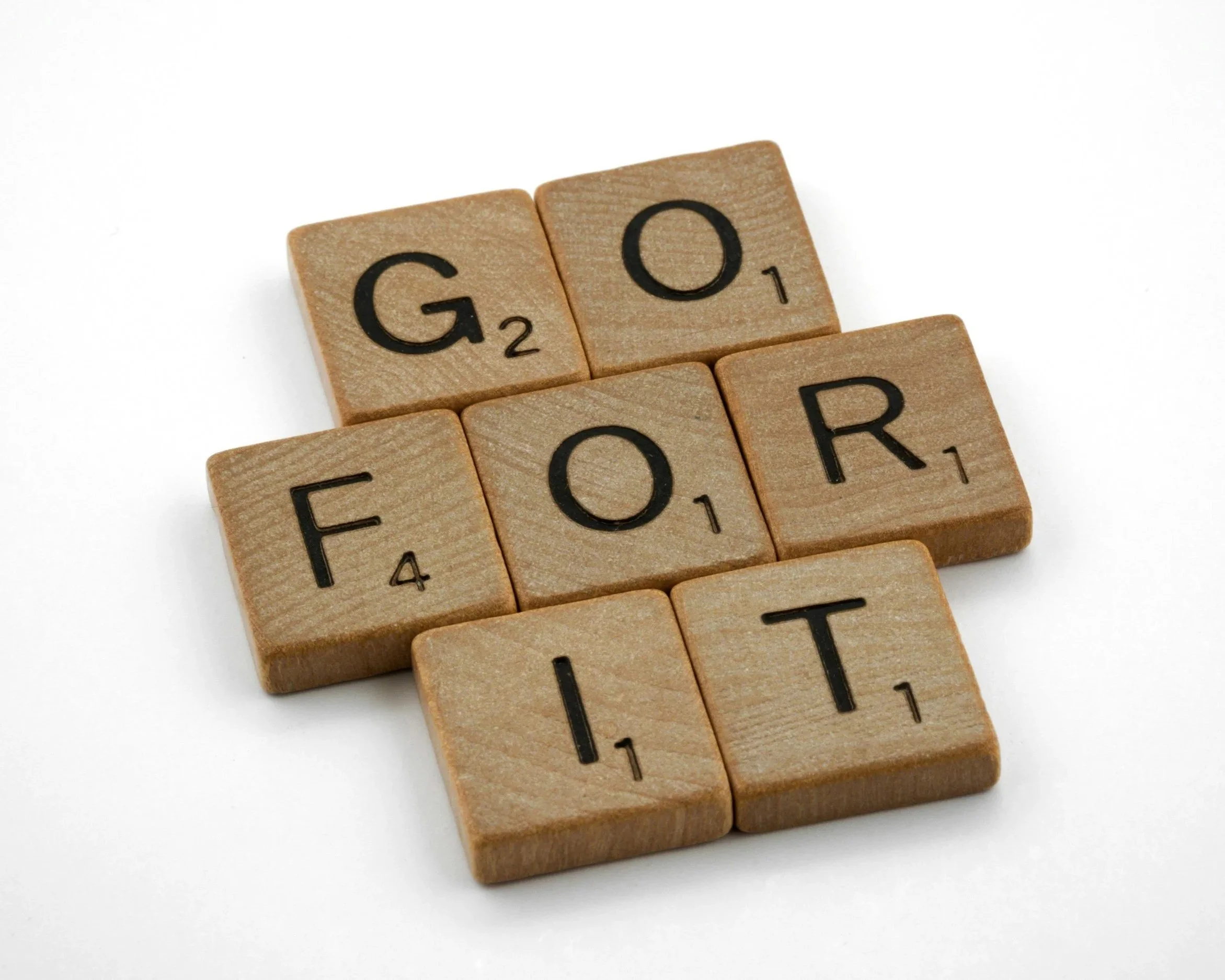 Close-up of wooden Scrabble tiles spell out 'GO' and some other partially visible letters on a white background.