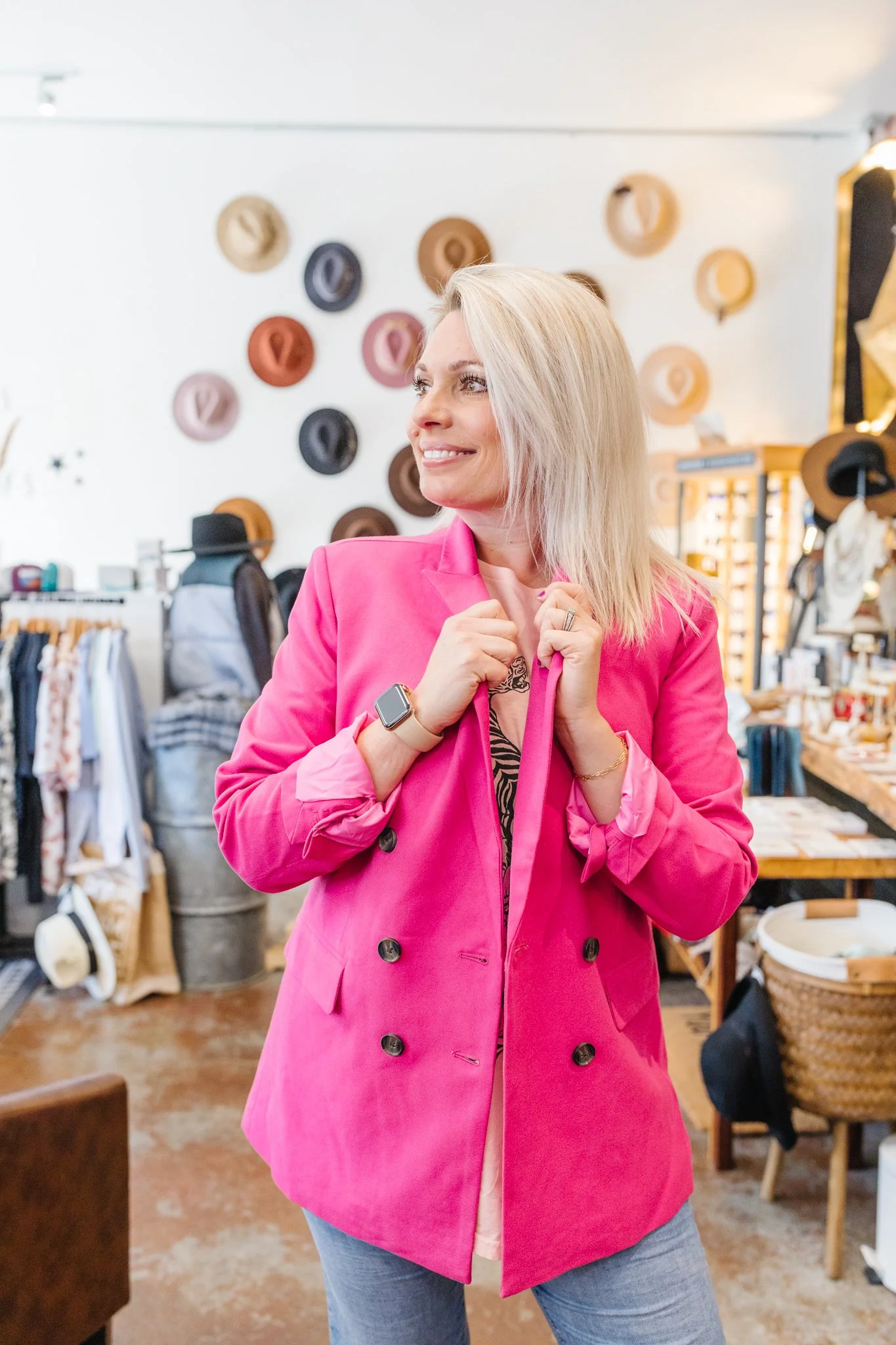 woman in a pink jacket shopping in a store with hats and accessories displayed behind her