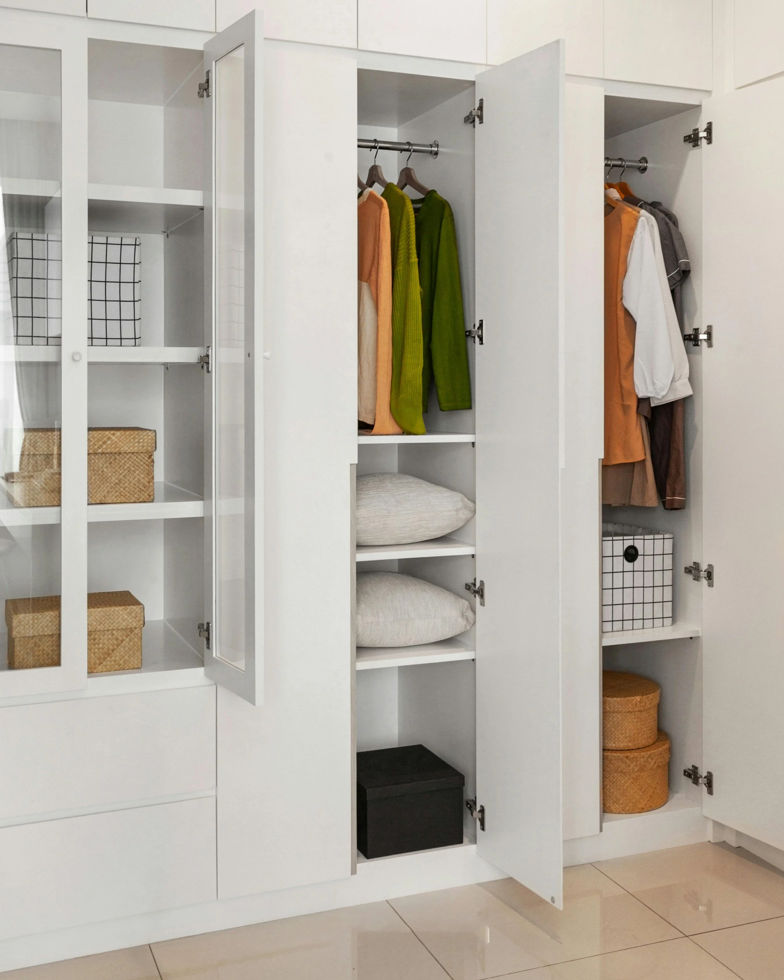 Open white storage cabinet with clothes hanging and storage baskets inside, situated on a tiled floor.