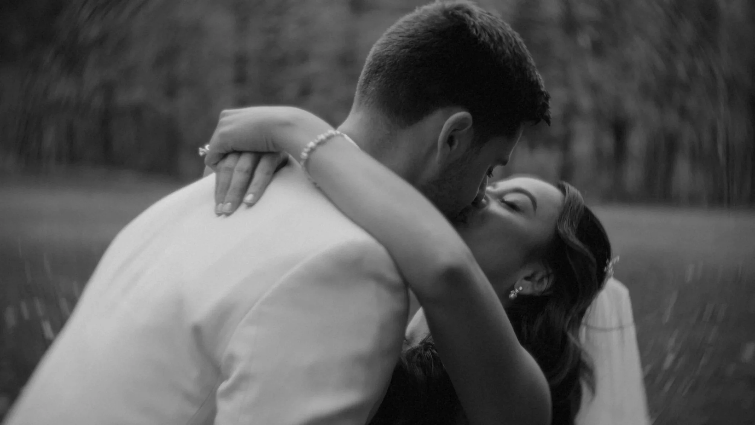 A couple embracing outdoors, with the man holding the woman as they kiss.