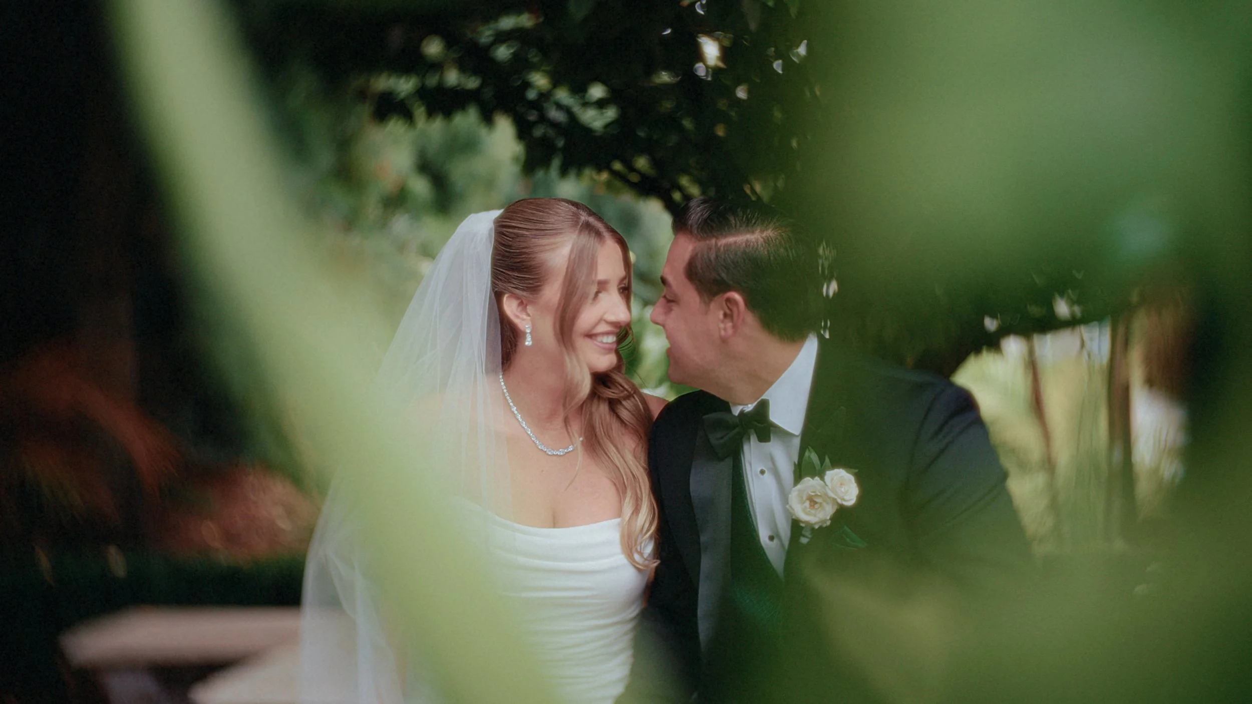 A bride and groom sharing a joyful moment during their wedding, surrounded by greenery.
