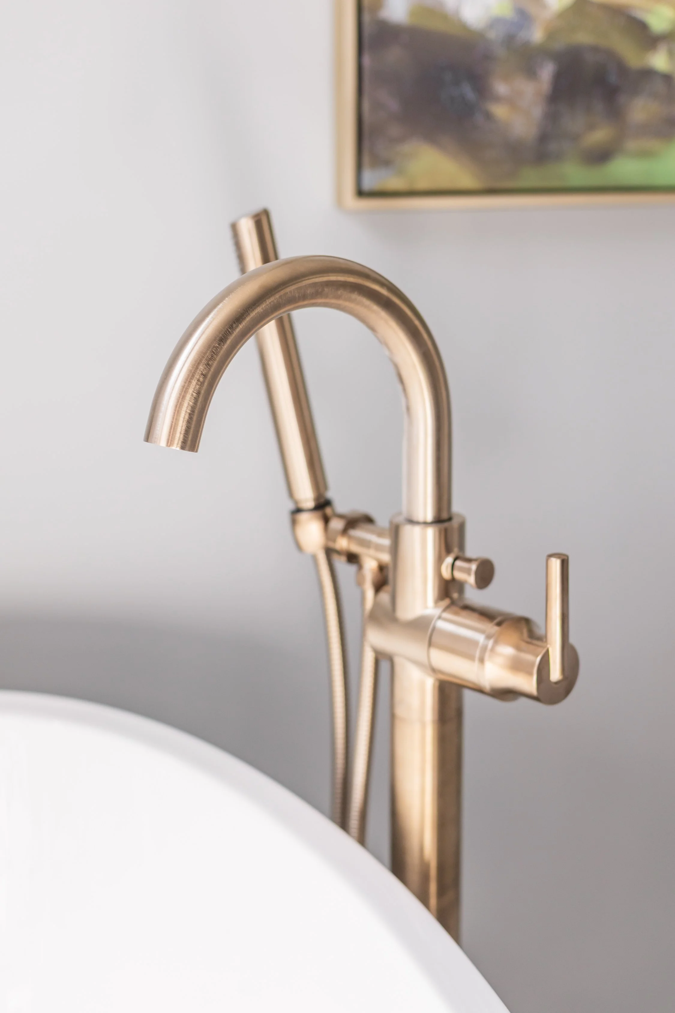 Close-up of a modern brushed gold kitchen faucet with a matching soap dispenser on a white countertop in a minimalist kitchen.