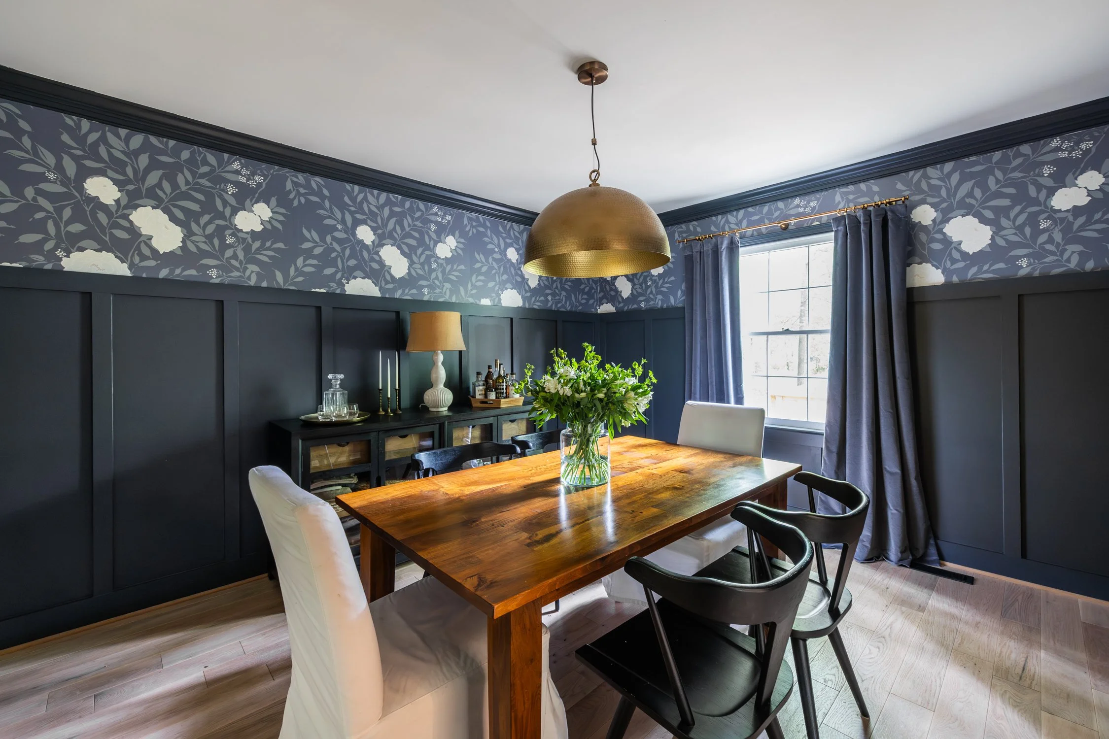 This 80's dining room is transformed with painted molding and coordinating wallpaper. The combination of navy, black, and brass give this an updated modern feel.